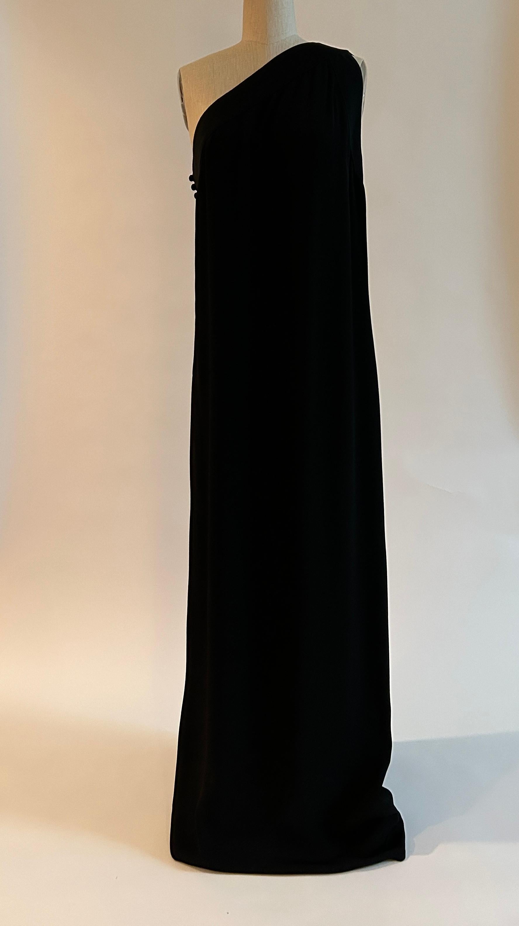 Vintage Adele Simpson black column style maxi gown with asymmetrical shoulder detailing. (Estimated circa 1970s, based on red and blue union label.) Straps fasten at one side and cross over shoulder to attach at two separate places at slightly