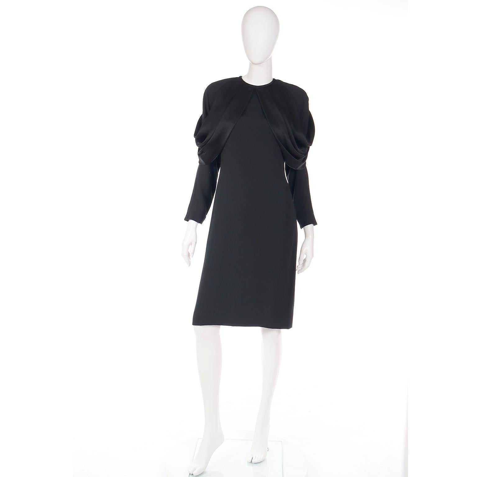Cette petite robe noire des années 1980 d'Adele Simpson a un superbe drapé sur chaque épaule ! Il a de longues manches raglan avec des pad pour structurer les épaules, et deux pièces de satin qui commencent de chaque côté du centre de l'encolure,
