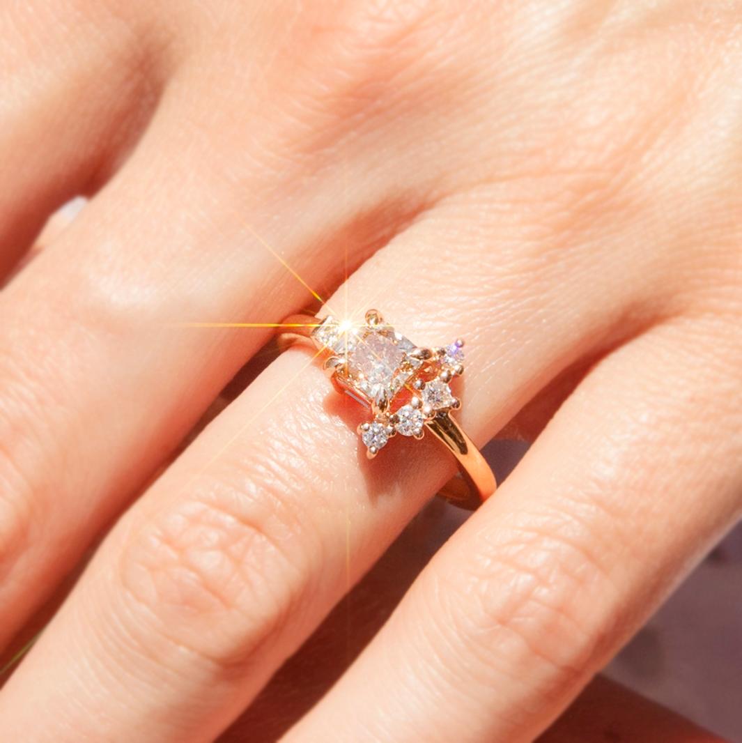 Lovingly forged in 18 carat rose gold, this gorgeous ring is a ravishing contemporary wonder! A gleaming rose gold band rises to a stunning fan-shaped cluster setting. At the centre is an enchanting ADGL-certified cushion cut cognac diamond with a