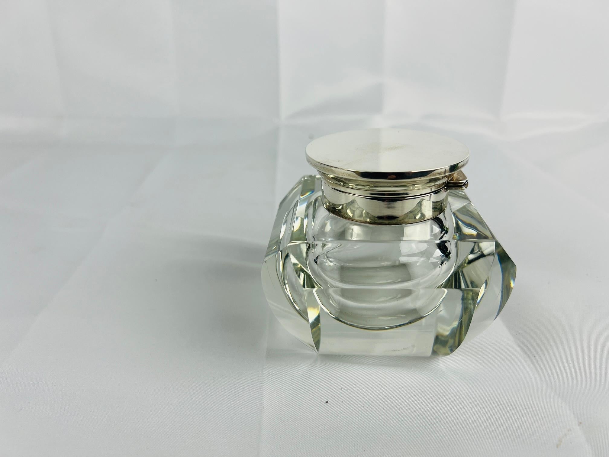 Ce pot de toilette ou encrier raffiné, fabriqué par la société réputée Adie Brothers Ltd, témoigne de l'élégance intemporelle du design britannique du milieu du XXe siècle. La pièce présente un corps en cristal magnifiquement taillé, orné de motifs