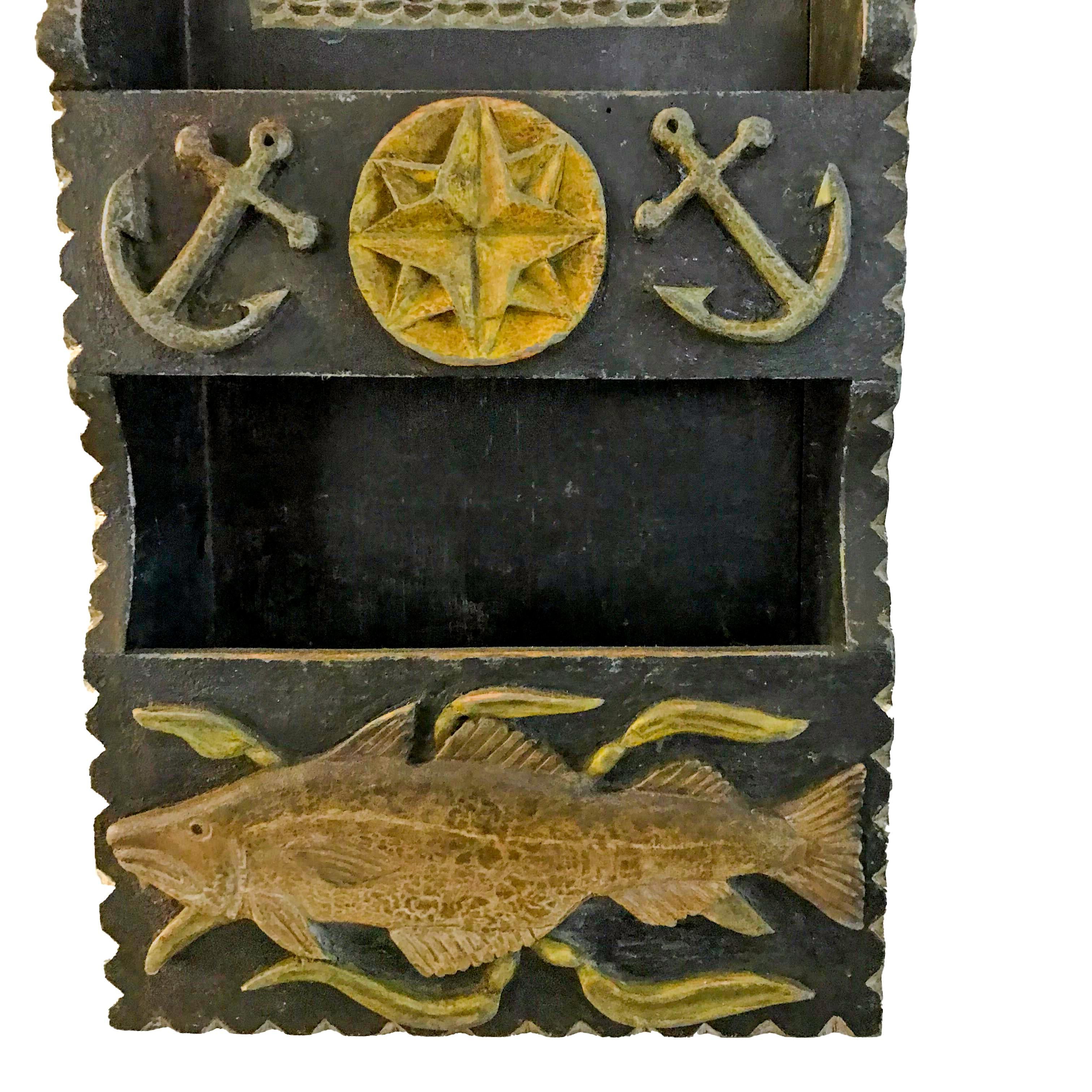 Hanging wall box, carved from pine, with two pockets, the ship is carved in relief and the fish, leaves, compass and anchors are applied. The edges are chip carved and painted white with a pierced lollipop backboard. The sides have a great alligator
