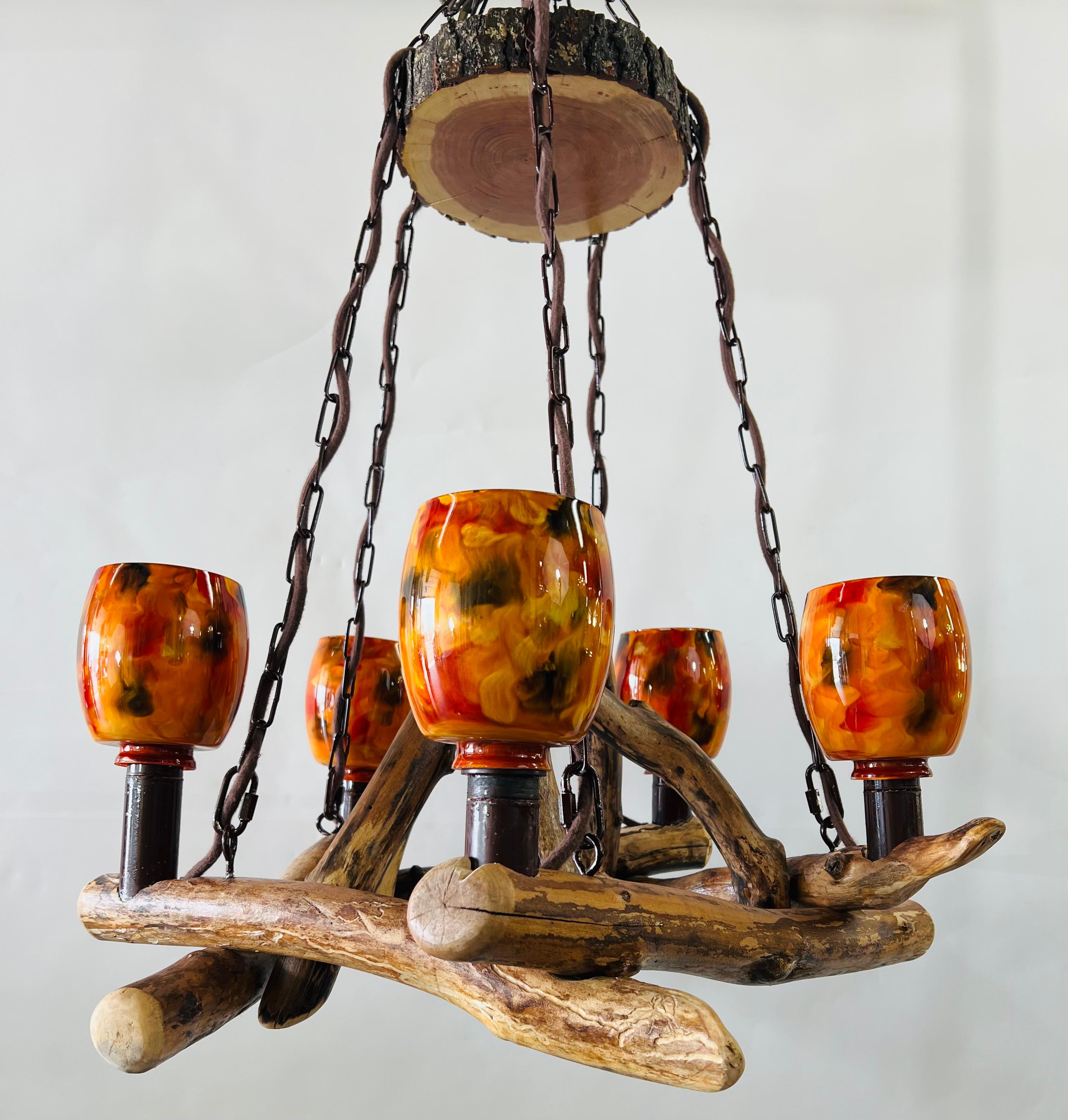 A stylish and one of a kind rustic Adirondack style chandelier with custom orange hurricane glass shades. In an organic modern design, the chandelier has four Maple wood logs forming a square shape and hanging with 4 chains. The chandelier body dish