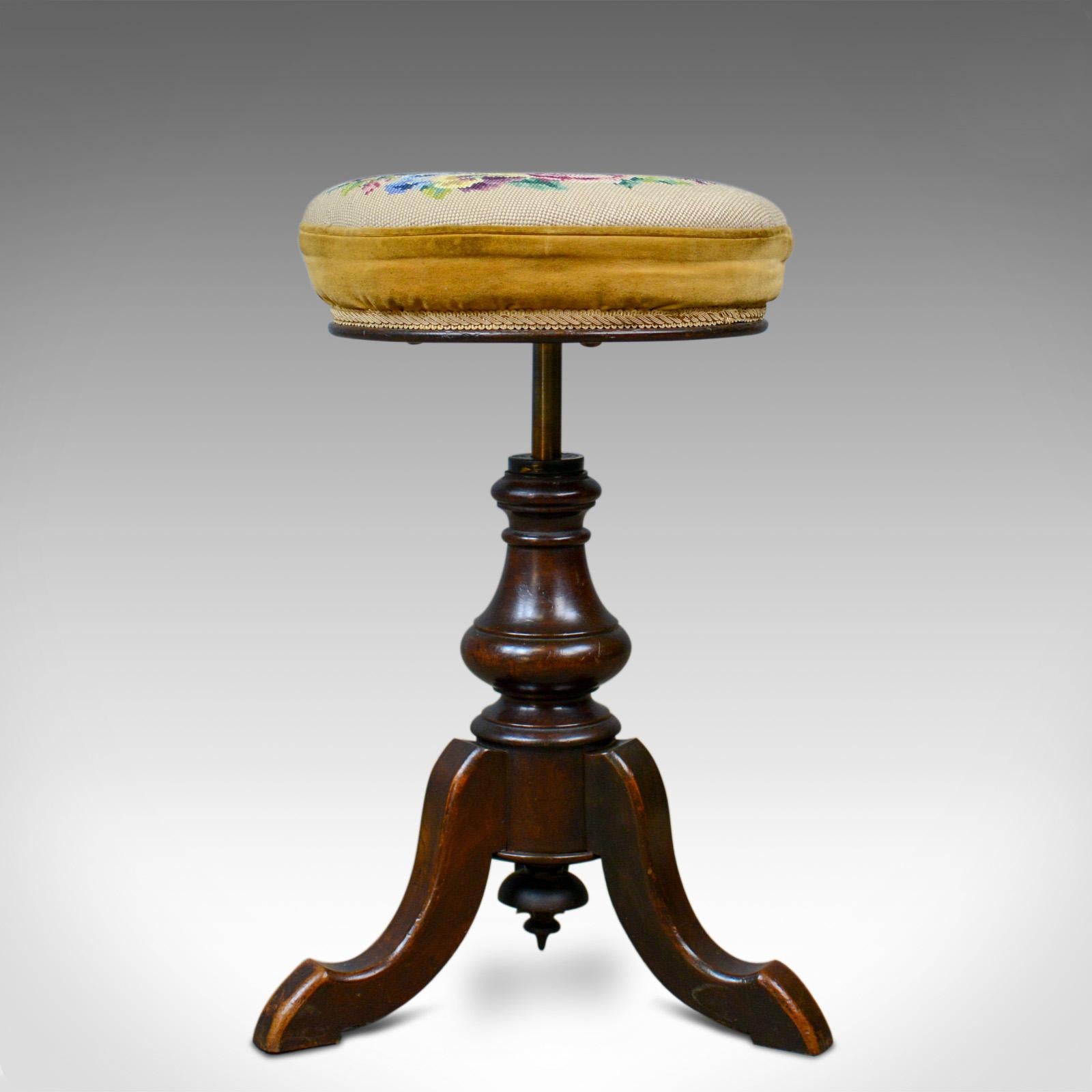 This is an adjustable, antique piano stool. An English, Victorian, walnut music stool with needlepoint tapestry seat pad dating to the latter part of the 19th century, circa 1880.

Beautifully made in solid walnut with a waxed finish and desirable