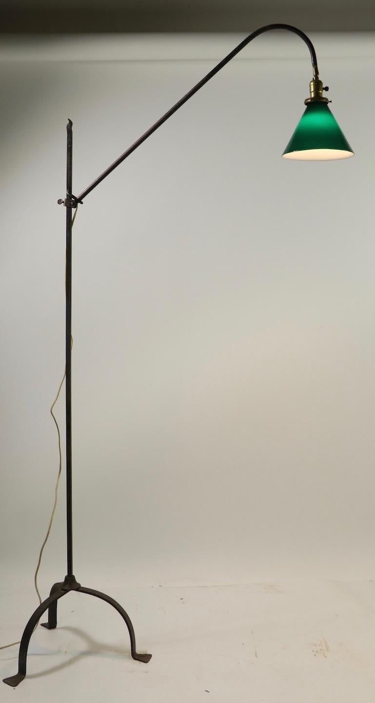 Wonderful wrought iron floor lamp having an adjustable arm which supports a green and white cased glass shade ( unsigned Emeralite ). The floor lamp has a tripod base, and vertical standard, the standard ( vertical post 58.25 inch H ) supports an