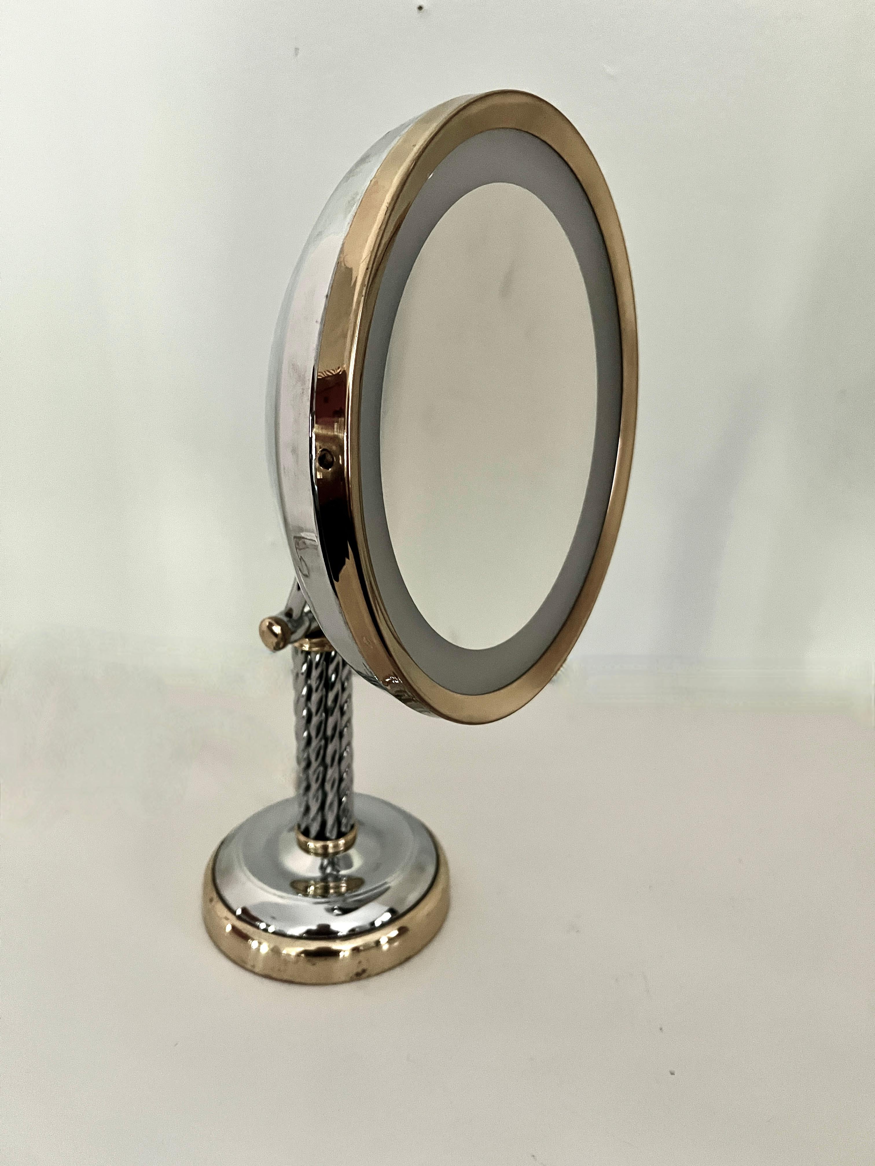 A beautifully designed Magnification Mirror with surrounding light.  The Piece is in very good condition with a Braided Chrome stand.  
The brass and chrome details give this piece an artistic sophistication, allowing one to leave it on the counter