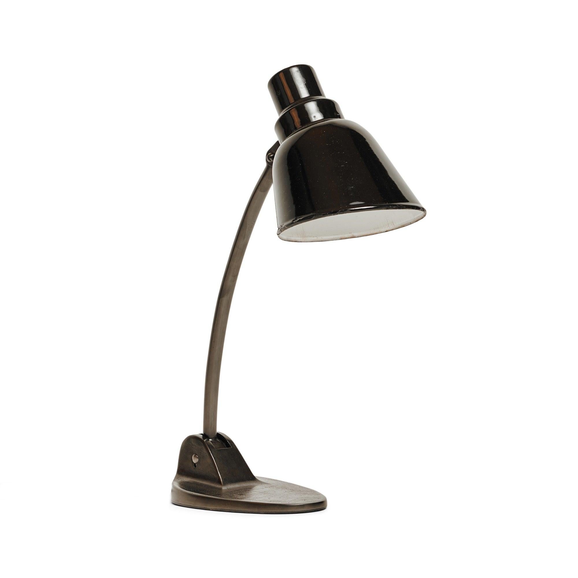 An adjustable and articulated industrial desk lamp in patinated brass having a stepped base and swiveling conical shade.