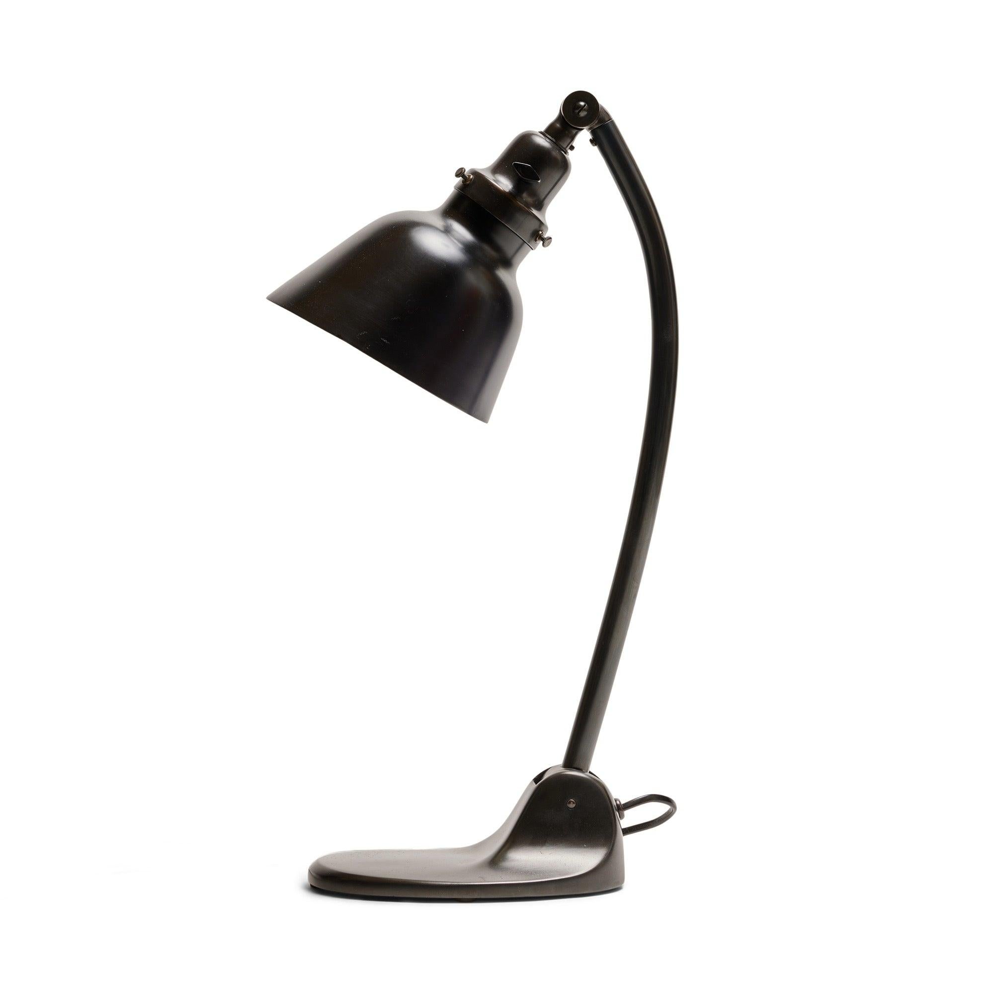 An adjustable and articulated industrial desk lamp in patinated brass having a stepped base, conical shade and exposed tension bars.