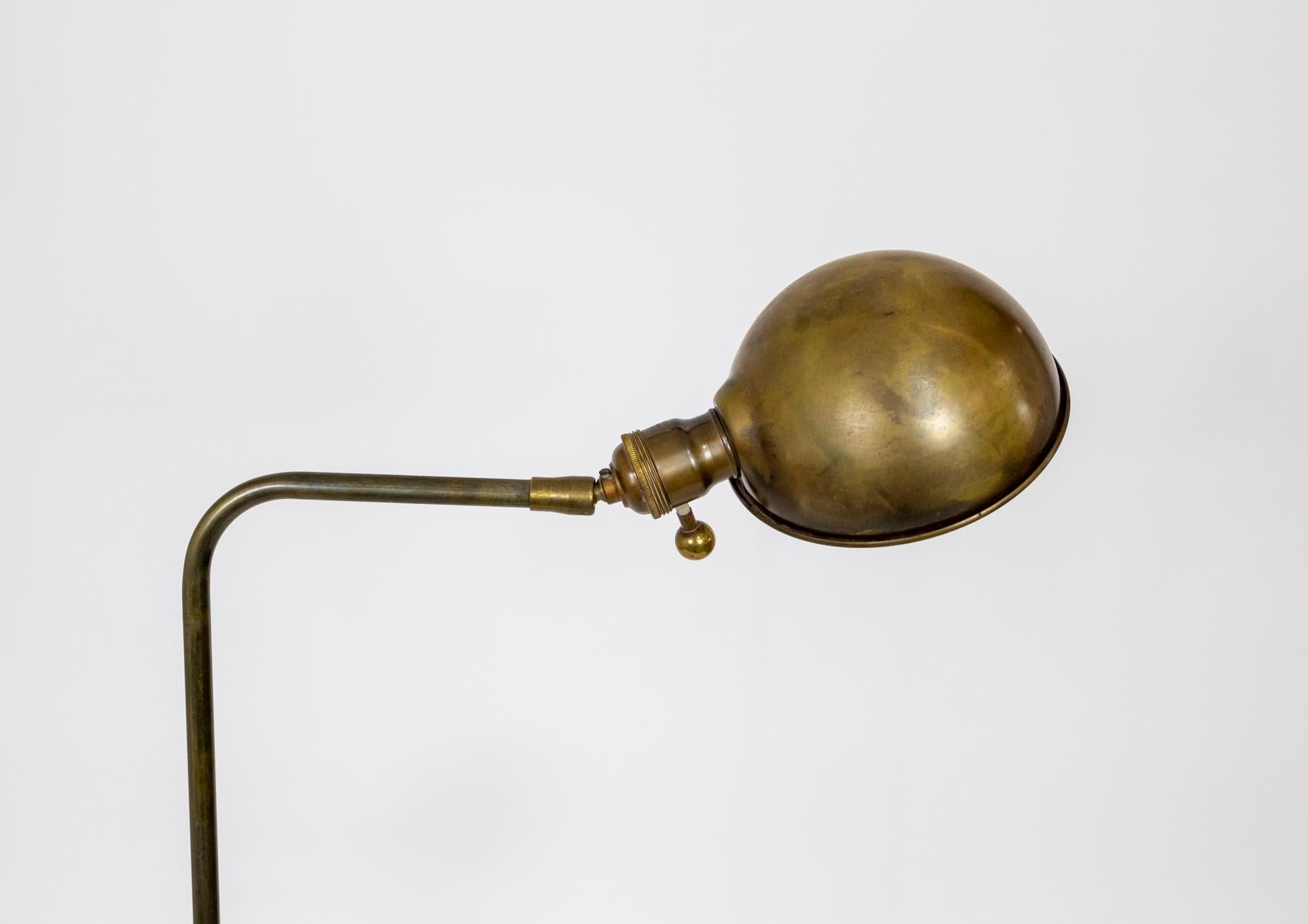 An antique, pharmacy style floor lamp with a dome shaped shade and ball knob on the socket. In richly patinated brass, with the shade interior lacquered white. Adjustable shade angle and height, with weighted base and dimmer (medium base) socket.