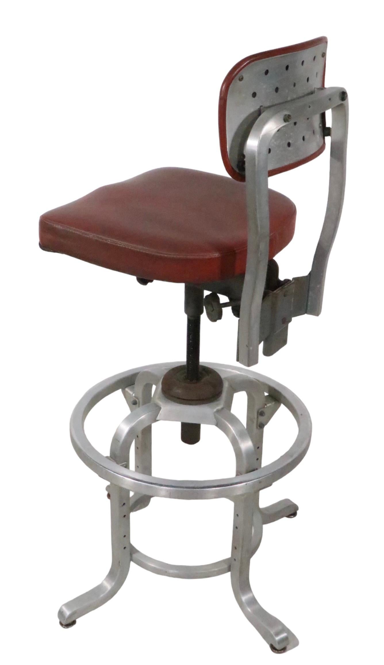 Classic Industrial, Mid Century, Machine Age style drafting stool by General Fireproofing, Good Form. The stool has  a squared aluminum frame structure, vinyl seat and back rest. It features several adjustments, as follows:
Back Rest raises and