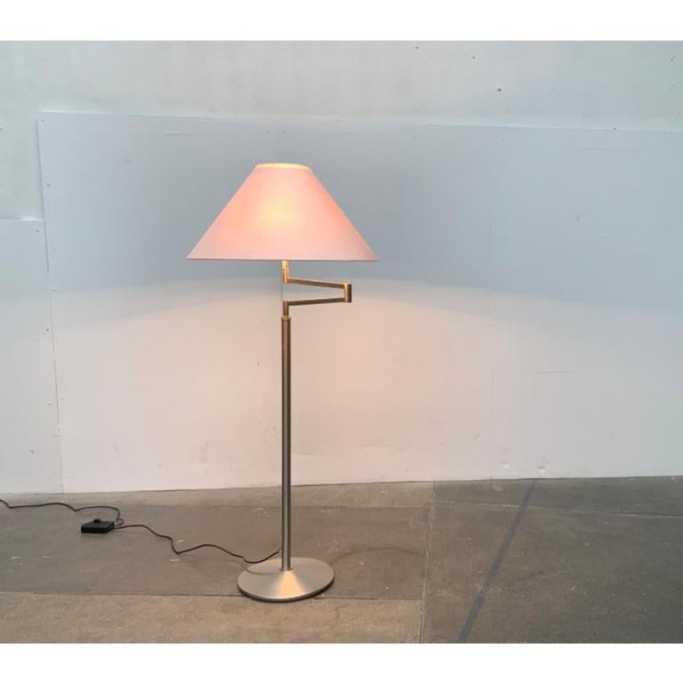 Elegant floor lamp with height adjustment and swivel arm.

The lamp has a simple, conical shade with fabric covering. The screen sits on a swivel arm. The shaft is divided into two and ends in a round base. The upper part can be adjusted in height