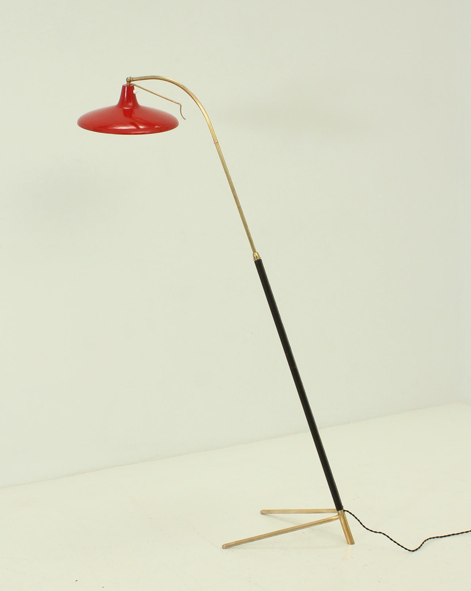 Adjustable italian floor lamp from 1950's. Shade in red enamelled metal with movable kneecap to adjust different positions, sterm in brass and black leather adjusted in height from 152 to 182 cm.
