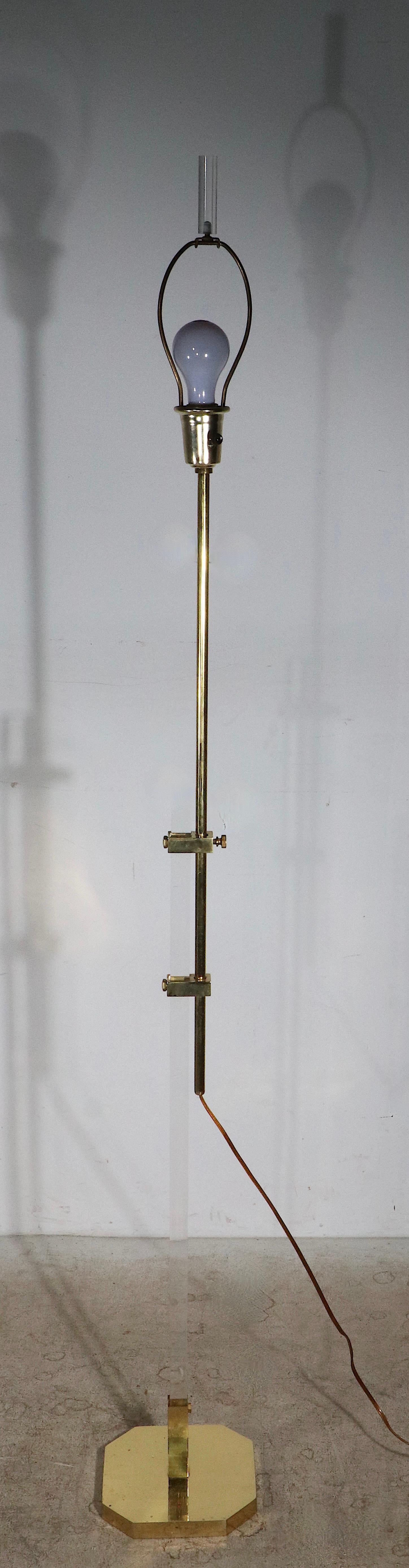 Chic adjustable floor lamp of lucite and brass. The lamp features a rectangular vertical shaft of solid transparent lucite on a six sided brass base, which is coupled with an adjustable tubular brass vertical shaft. The lamp is in very good,