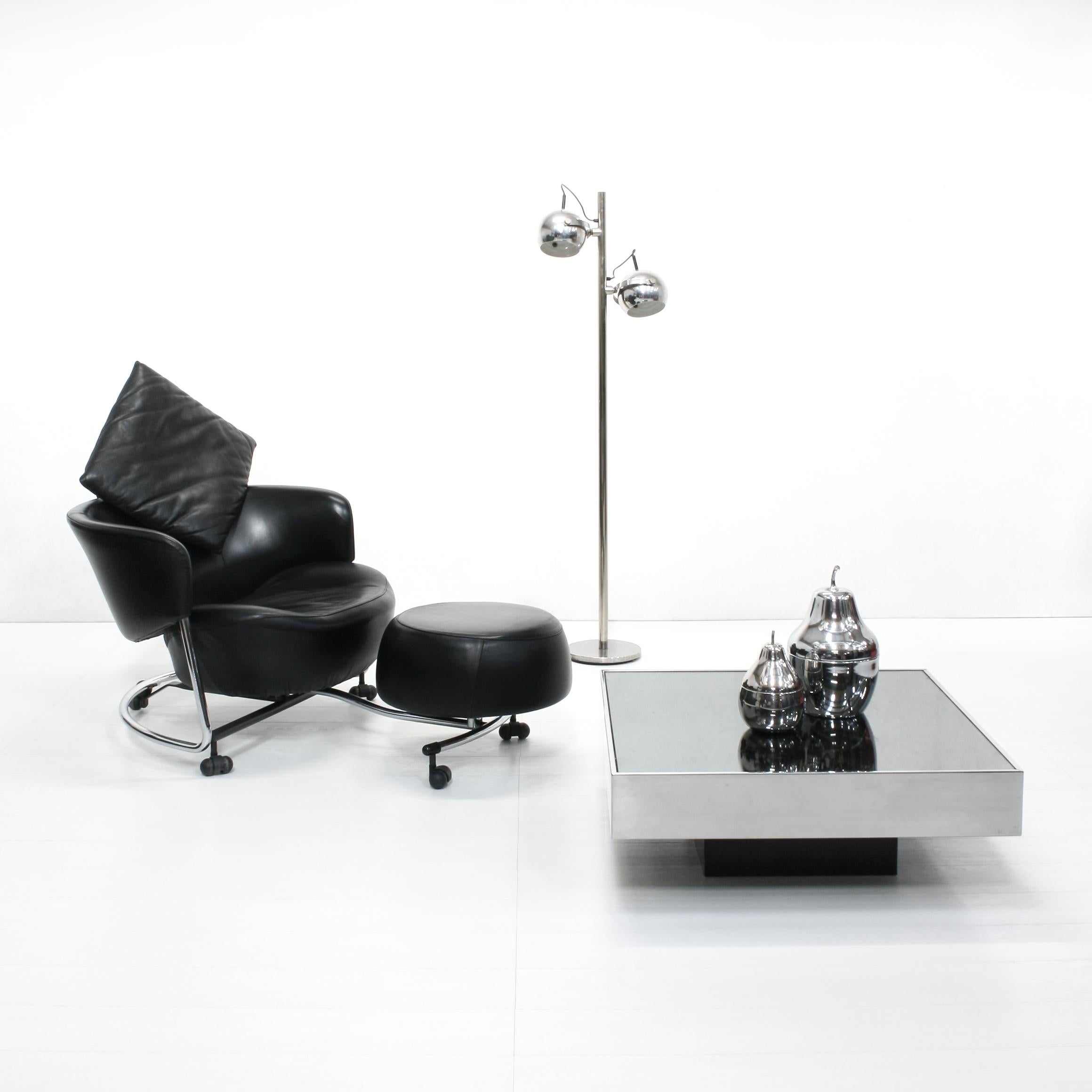 Fauteuil postmoderne en cuir noir sur une structure chromée avec siège, coussin d'appui-tête et ottoman satellite mobiles indépendamment. Le dossier est réglable en inclinaison.