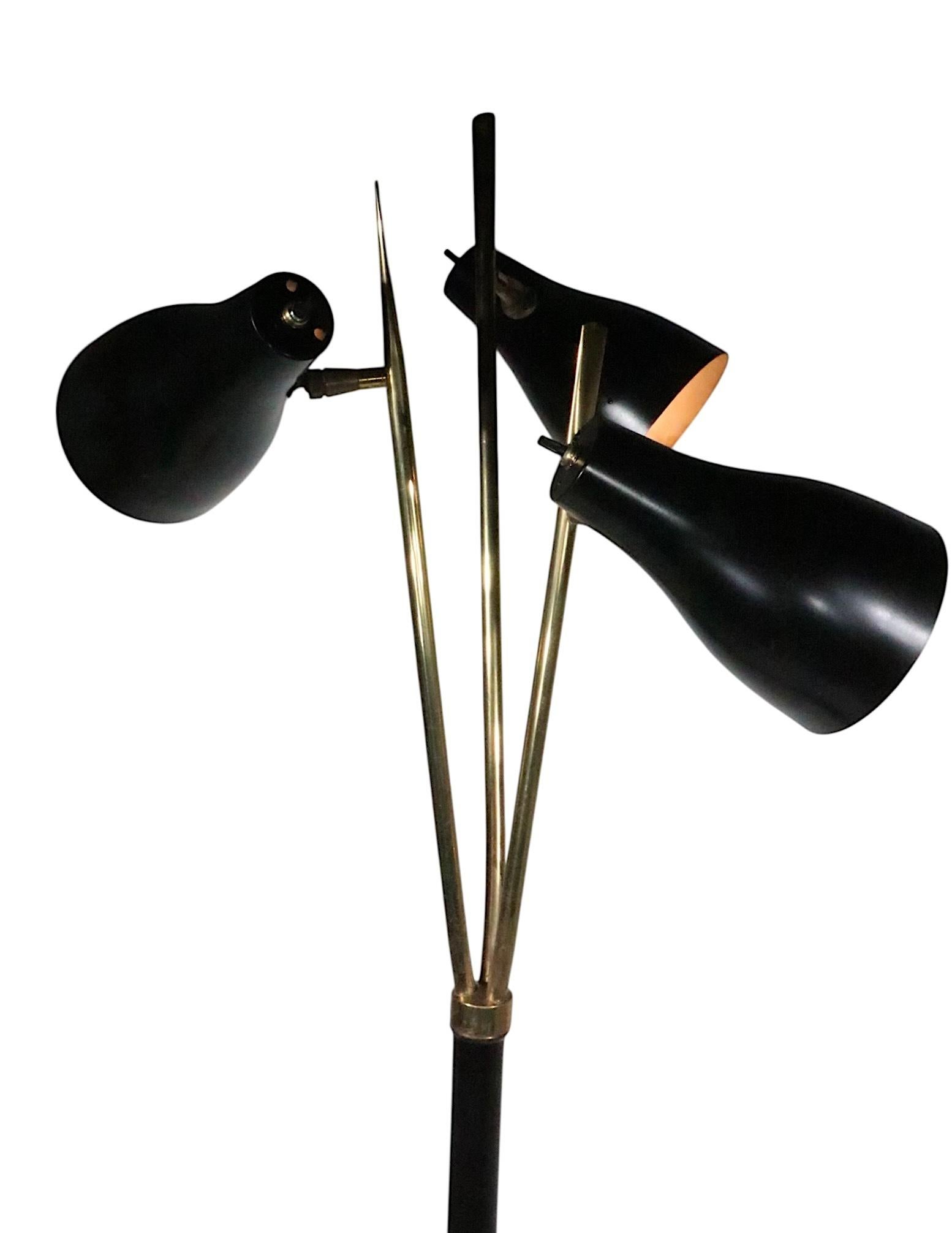 Classic Mid Century floor lamp, having three adjustable cone form shades mounted on spayed arms, a  vertical center pole, and disk form base. The lamp features a brass base and  black center  pole with brass trim, the shades are black, the arms are