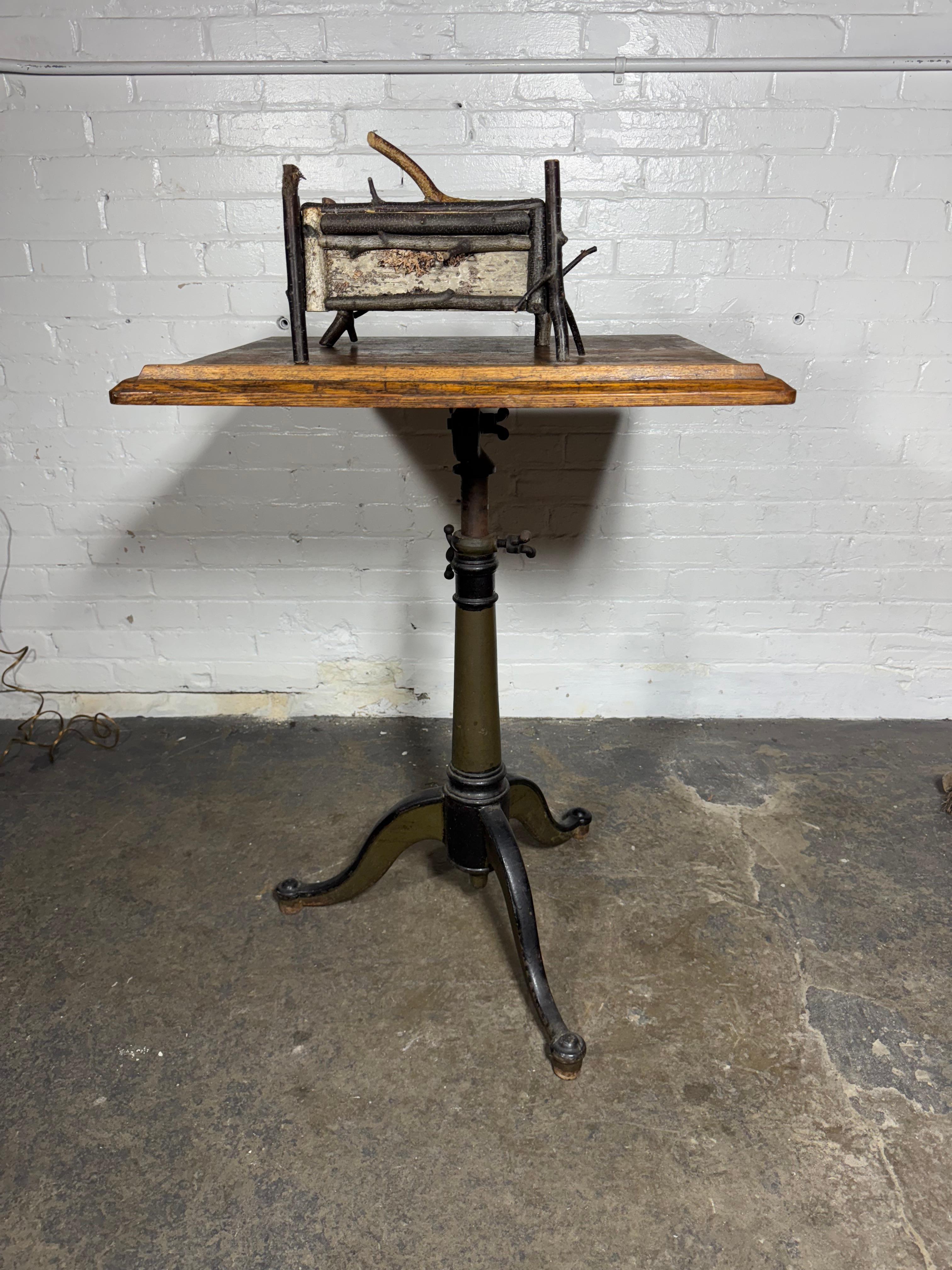An early 20th century cast iron and oak drafting table , The three-legged base adjusts up and down and the table top tilts, as well.Wonderful patina.great color. , Adjustable height from 3o