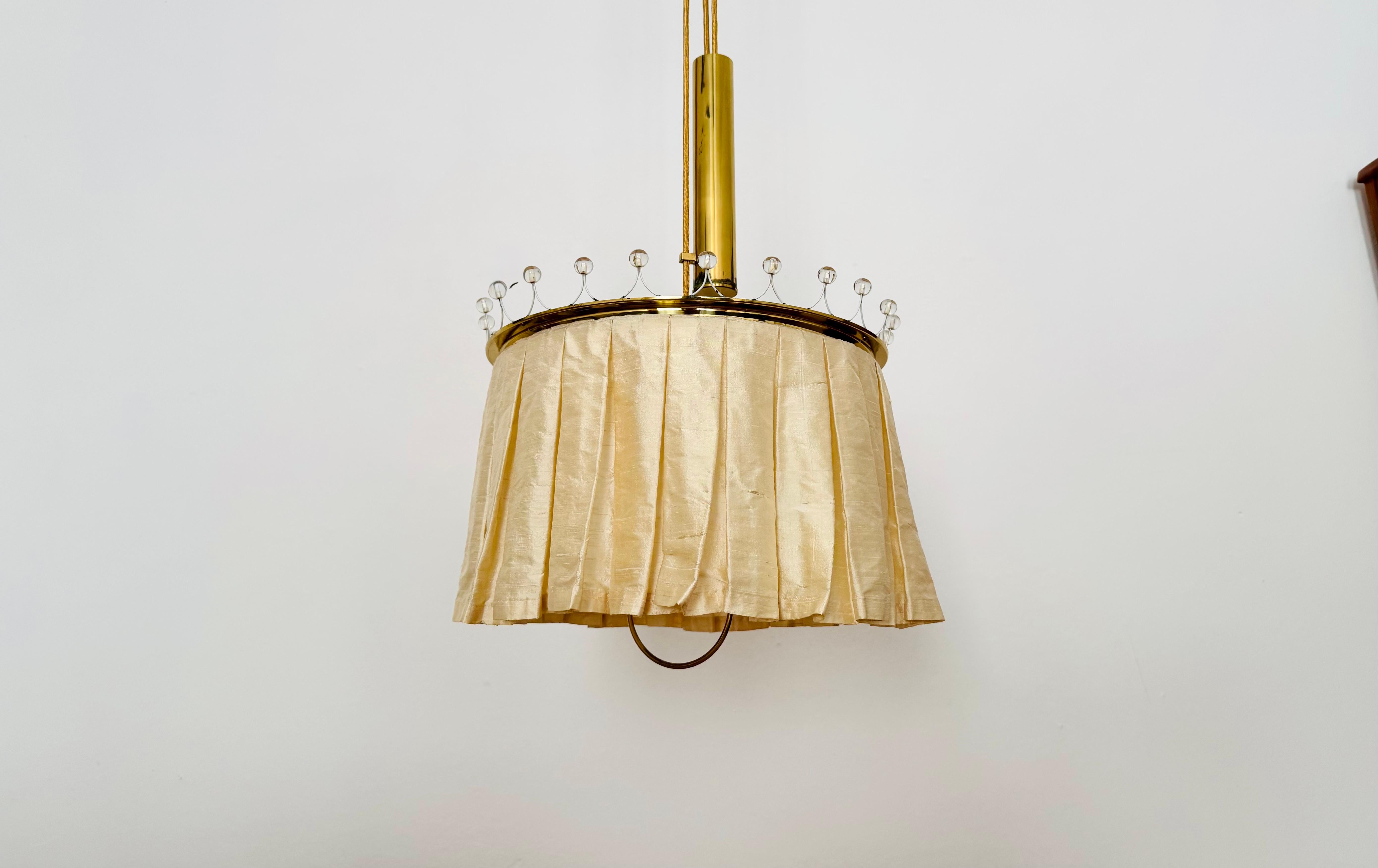 Very rare height-adjustable pendant lamp from the 1950s.
High-quality materials such as silk, brass, and crystal glass make this lamp a unique design object.
It creates a very cozy light.

Manufacturer: Vereinigte Werkstätten