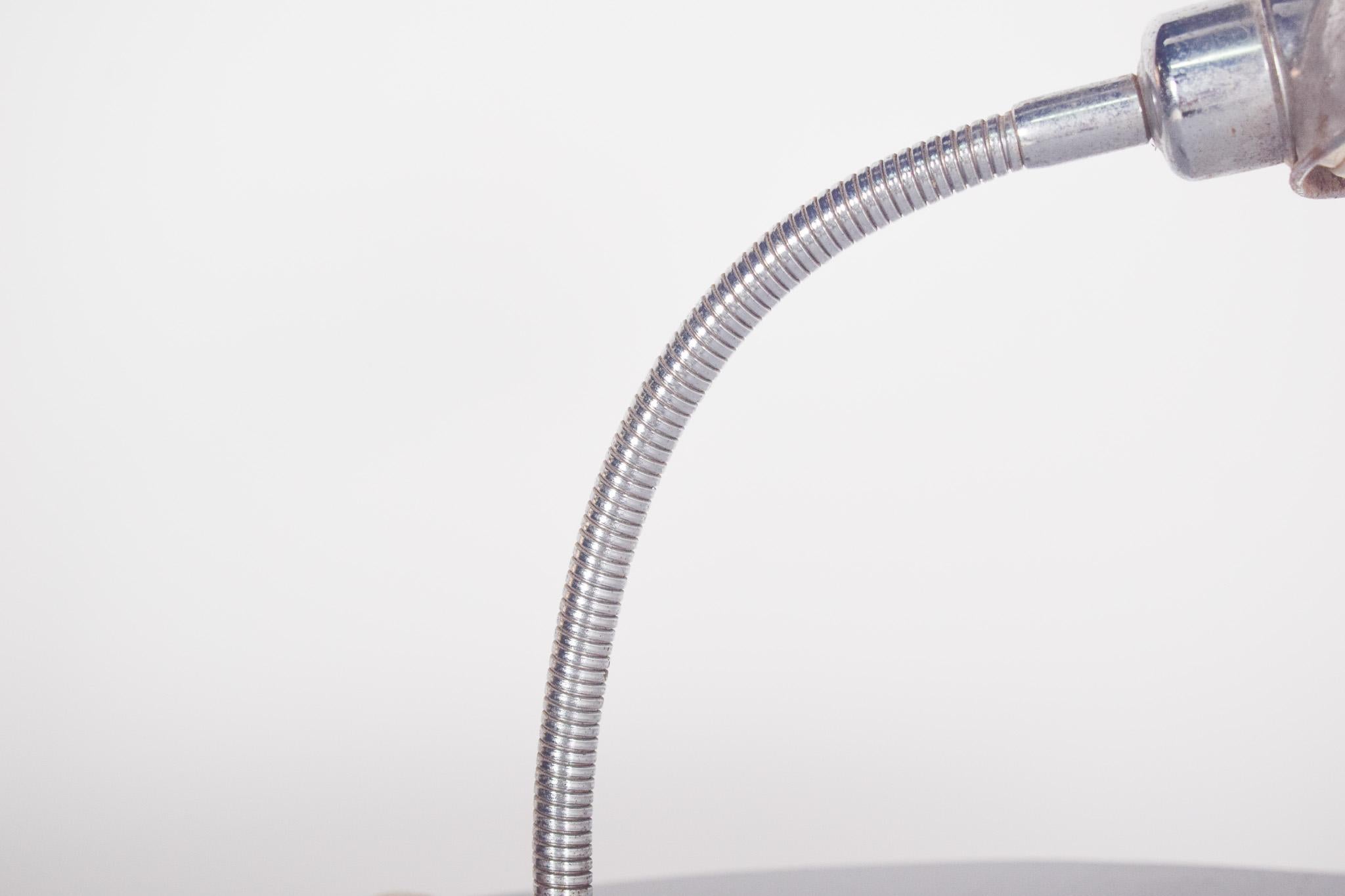 Lampada da scrivania vintage. Con una struttura in metallo e un design funzionale, il suo corpo principale è composto da una base circolare in metallo cromato, che ospita il pulsante che lo accende e lo spegne. Lo stelo flessibile, coperto da un