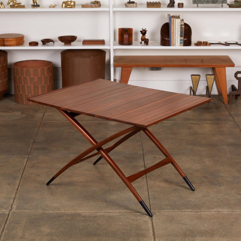 Edward Wormley’s design for an adjustable coffee or dining table, the Dunbar Model 5239, has an arcing X-shaped base and a tongue-and-groove walnut tabletop with a slight lip at either end. The table is adjustable with nine possible height