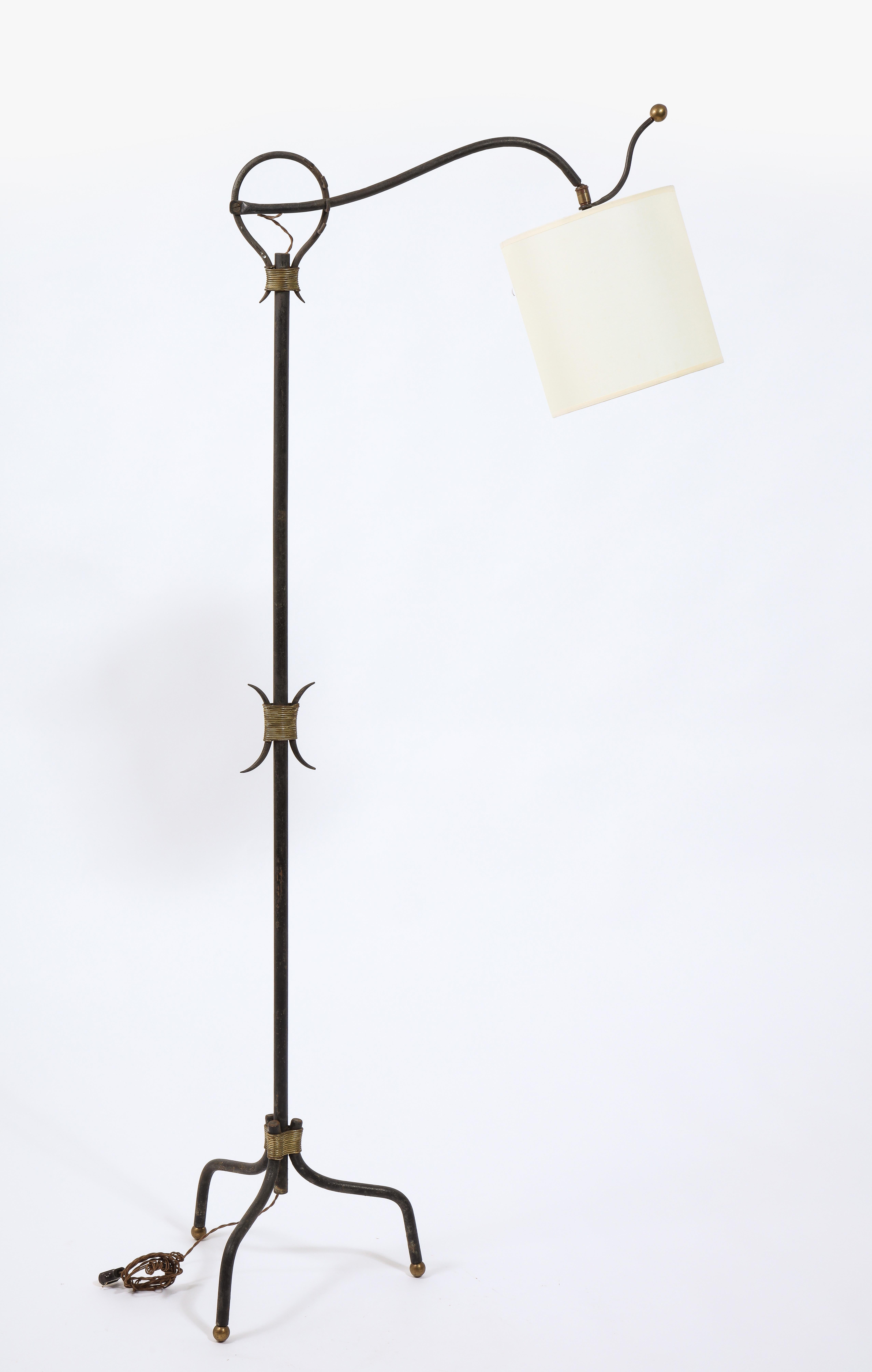 Adjustable tripod wrought iron floor lamp with brass accent and paper shade.