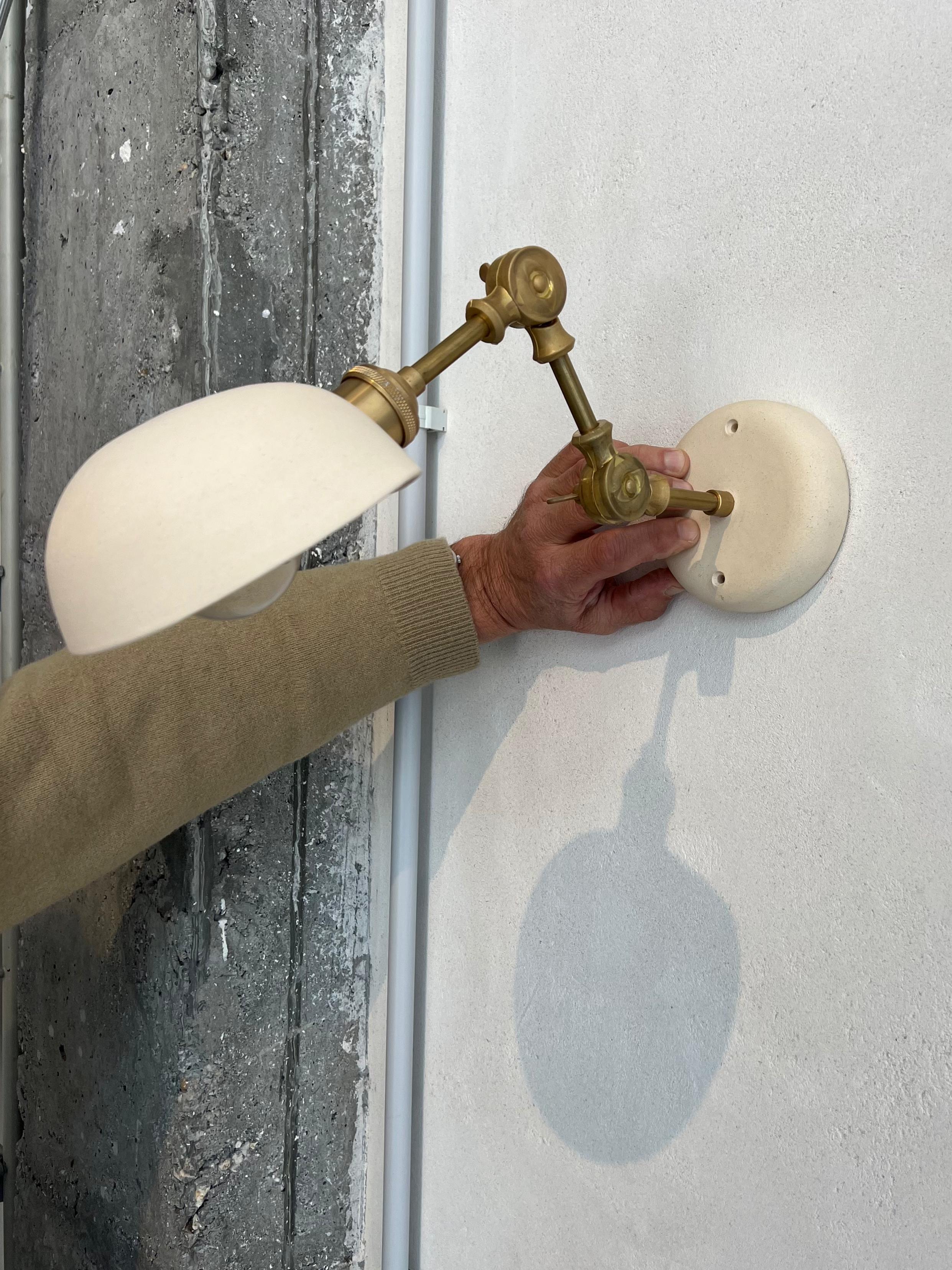 Wall sconce made from two pieces of broken, matte white ceramic. The ceramic is made in Buño, the most important artisan village in Spain and one of the most renowned in Europe. The brass pieces used are adjustable, making it the perfect sconce for