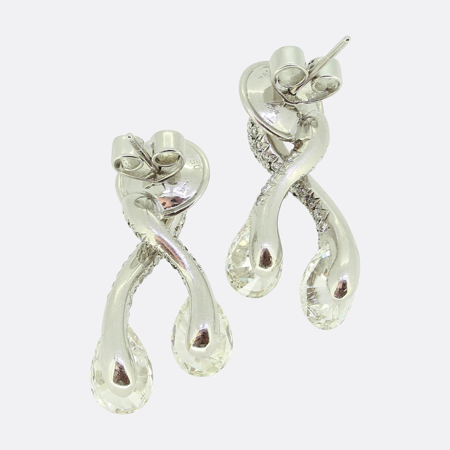 Here we have an exquisite pair of diamond drop earrings by Adler. Each earring features a graceful intertwining design, adorned with brilliant-cut white diamonds that cascade elegantly. The ends of the earrings are accentuated with pear-cut white