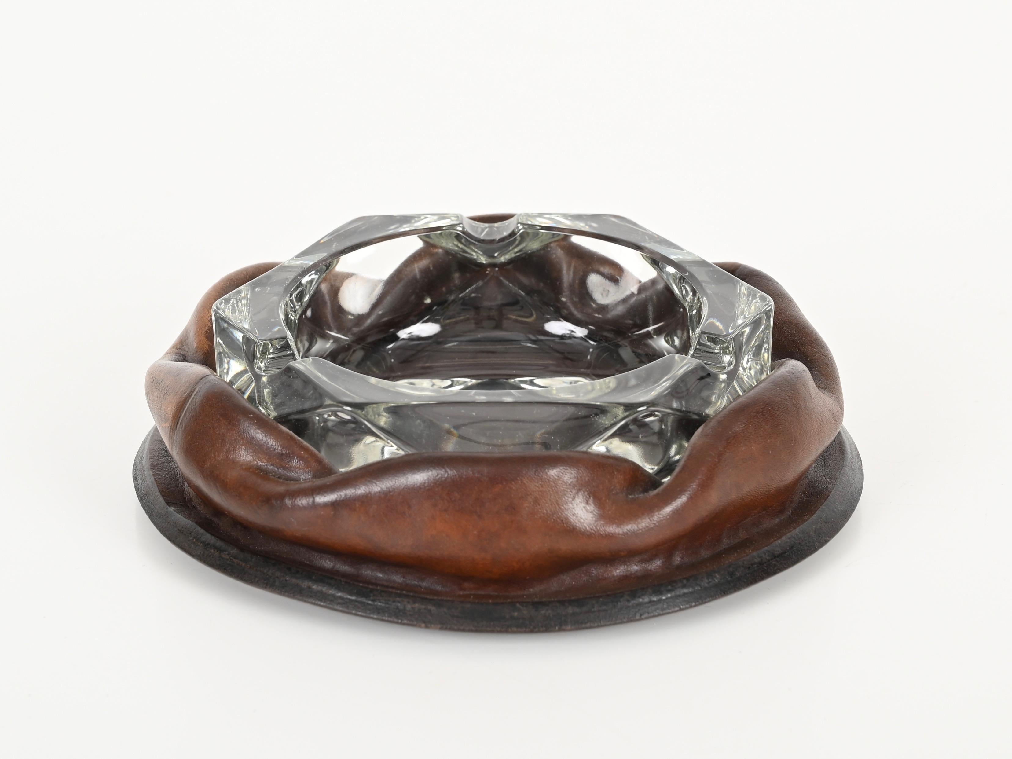 Meraviglioso posacenere di metà secolo in pelle marrone curvata e vetro di cristallo. Il design di questo posacenere incredibilmente elegante è attribuito alla maestria di Jacques Adnet ed è stato prodotto in Italia negli anni Cinquanta. È firmato