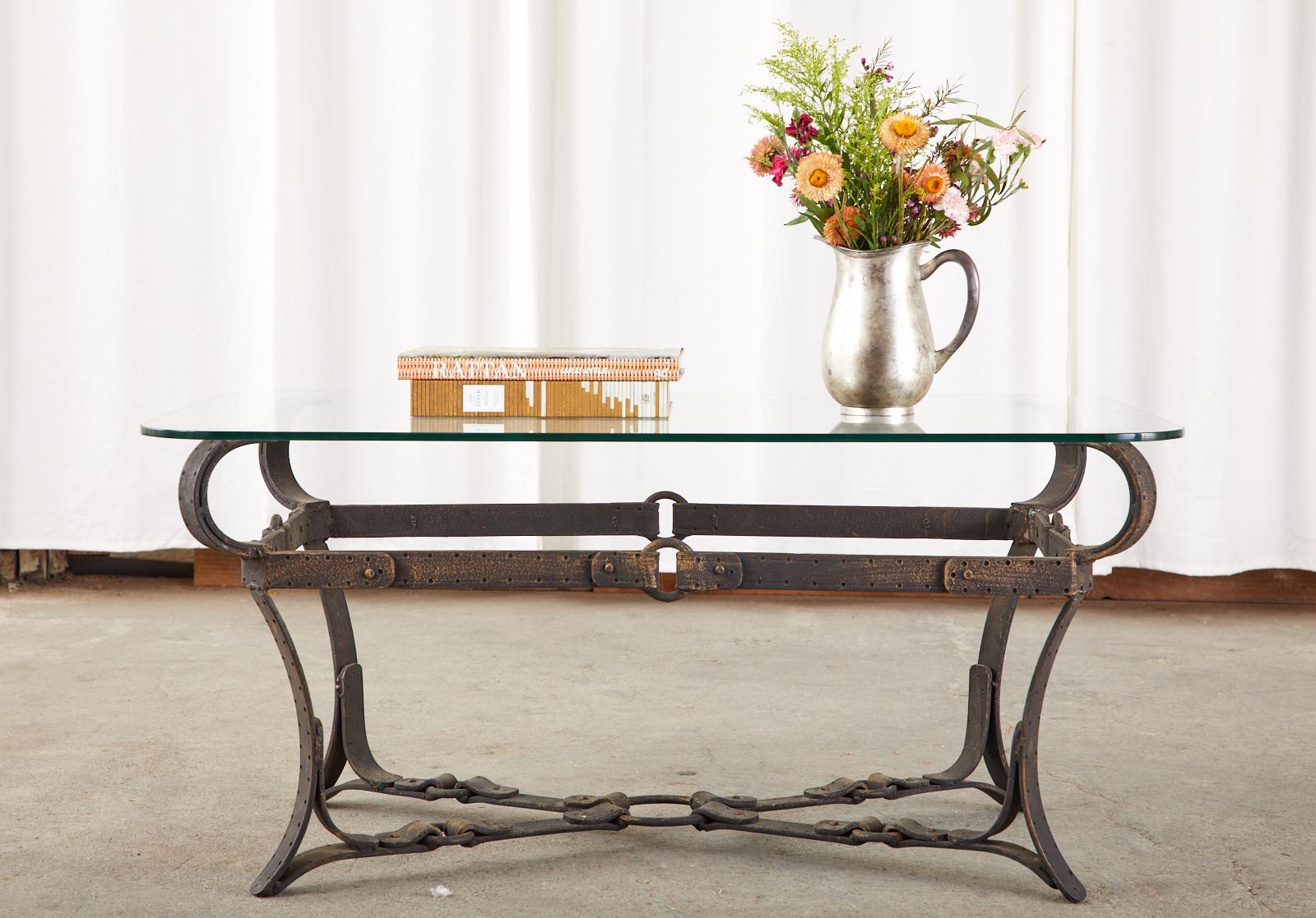 Mid-Century Modern cast iron coffee or cocktail table featuring a faux leather equestrian strap design in the manner and style of Jacques Adnet and Hermes. Beautifully crafted to resemble leather equestrian harness straps, rings, and buckles with a