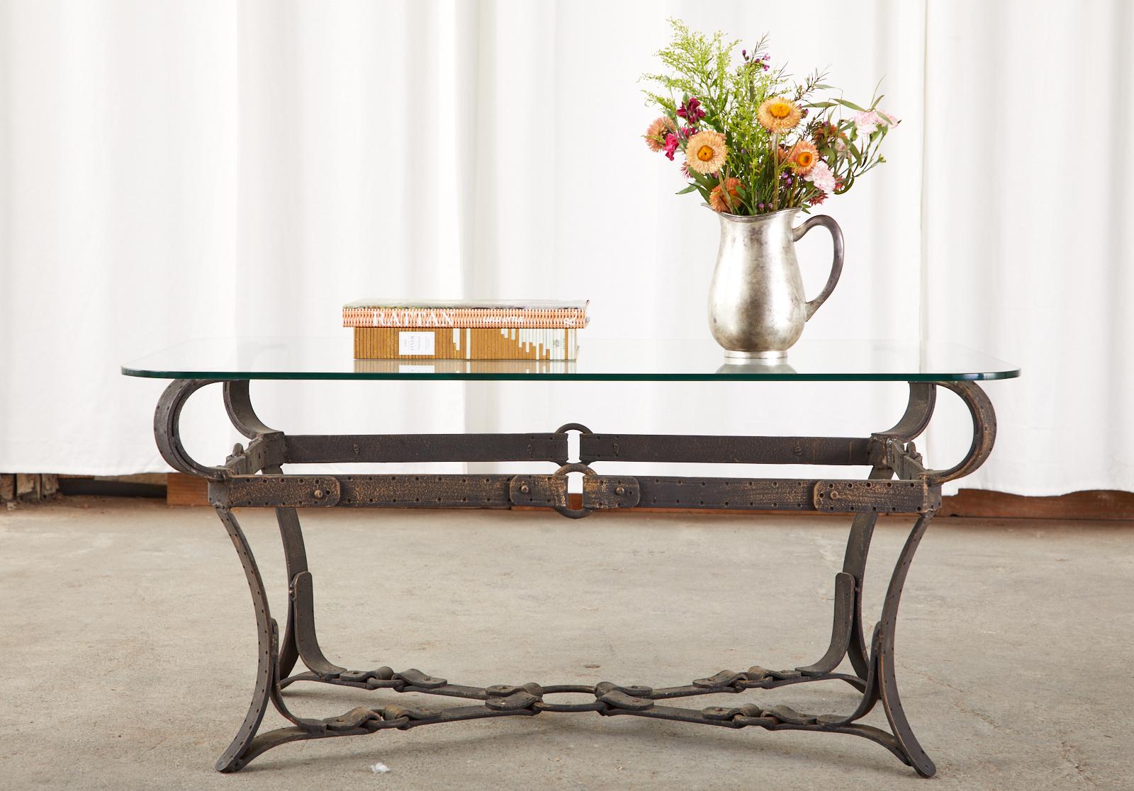 Mid-Century Modern cast iron coffee or cocktail table featuring a faux leather equestrian strap design in the manner and style of Jacques Adnet and Hermes. Beautifully crafted to resemble leather equestrian harness straps, rings, and buckles with a