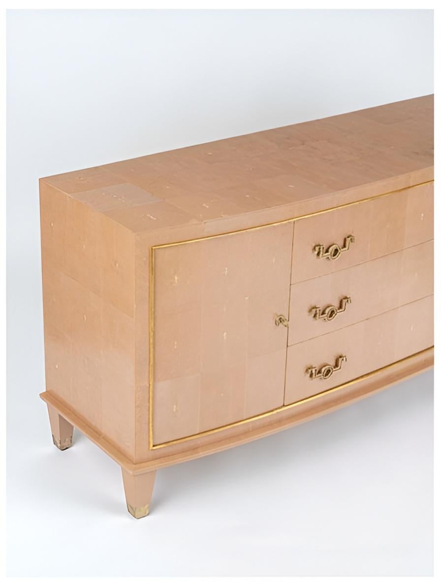A chest of drawers from oak wood, clad in shagreen with gilt bronze hardware and details, including the original gilt bronze keys. A slightly curved front features three central drawers with gilt bronze pull handles and are flanked by two doors to