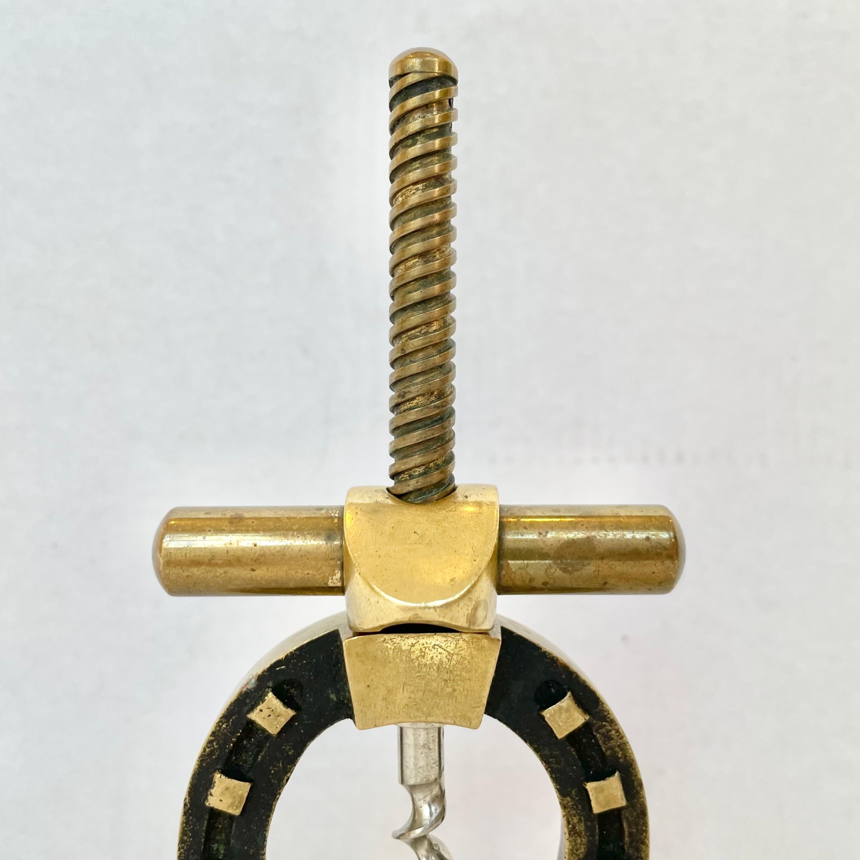 Brass bottle opener in the style of Jaques Adnet. Large screw runs the length of the corkscrew with a heavy brass grip and a sharp steel tip. With a beautiful and elegant design resembling a horseshoe, this piece is heavy and very solid. Stands up