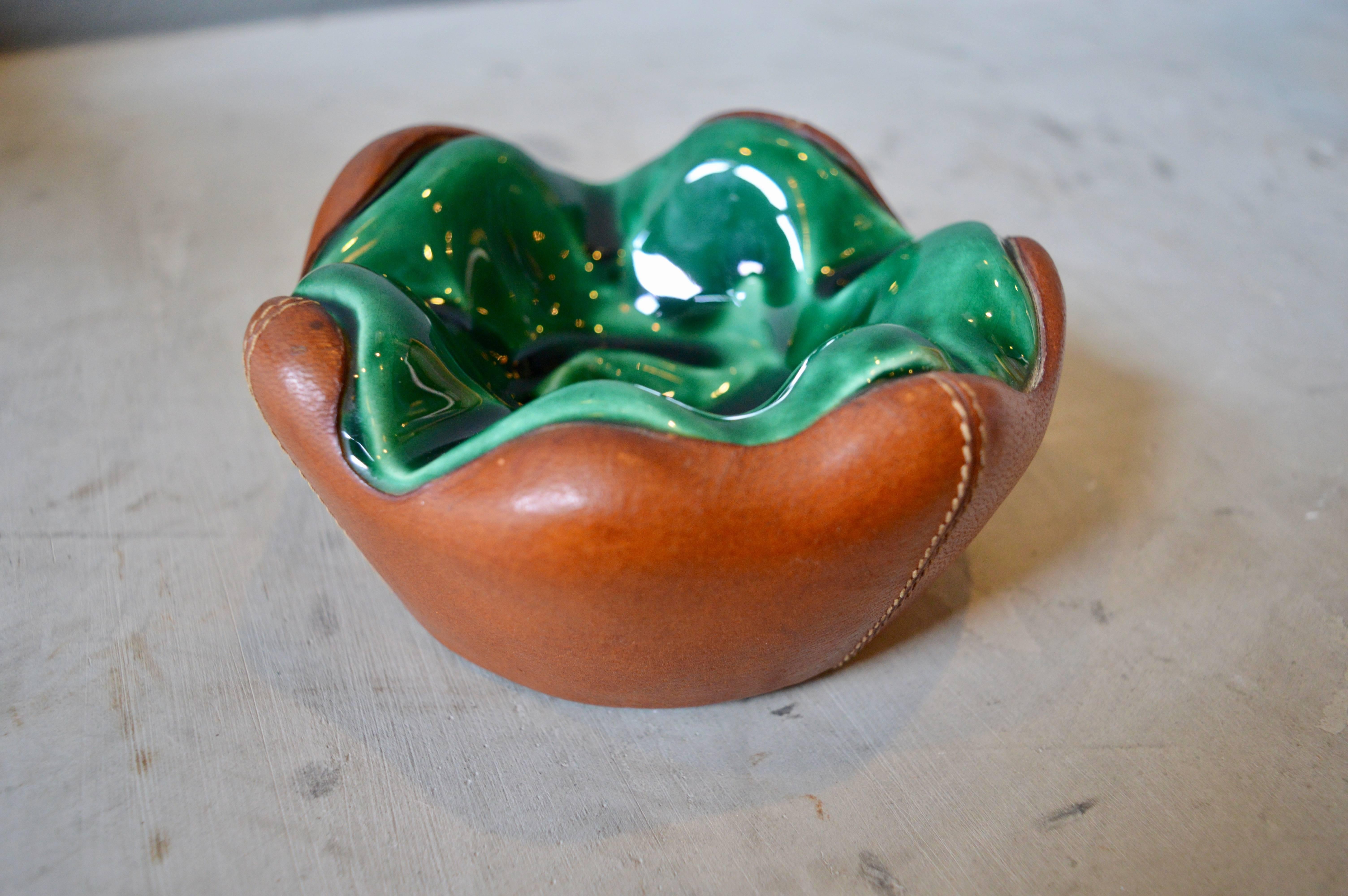 Handsome leather and ceramic ashtray or catchall in the style of Jacques Adnet. French saddle leather with hand stitching. Stunning green ceramic inset dish. Excellent vintage condition.