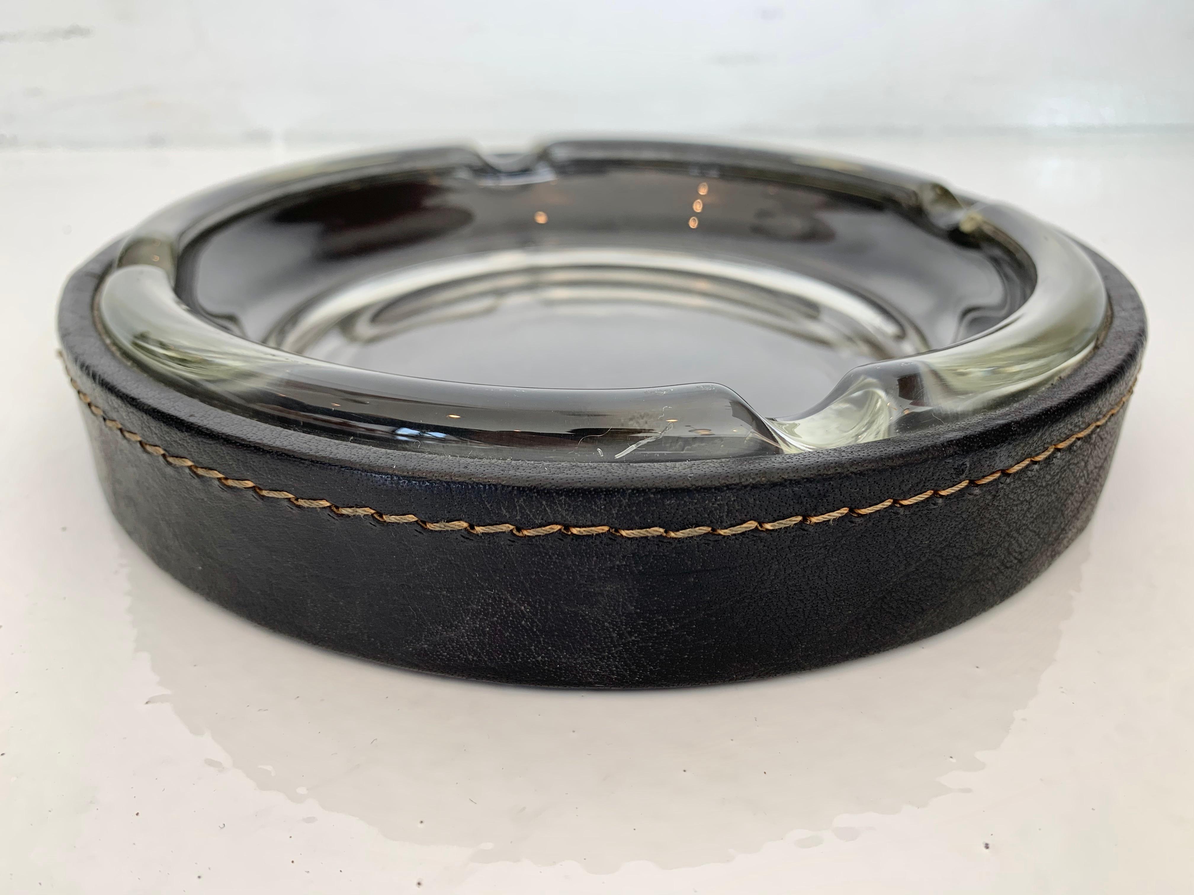 Handsome oversized black leather and glass ashtray / catchall in the style of Jacques Adnet. Contrast stitching throughout. Inset glass. Great desktop ashtray or catchall to put by the front door. Good vintage condition.
