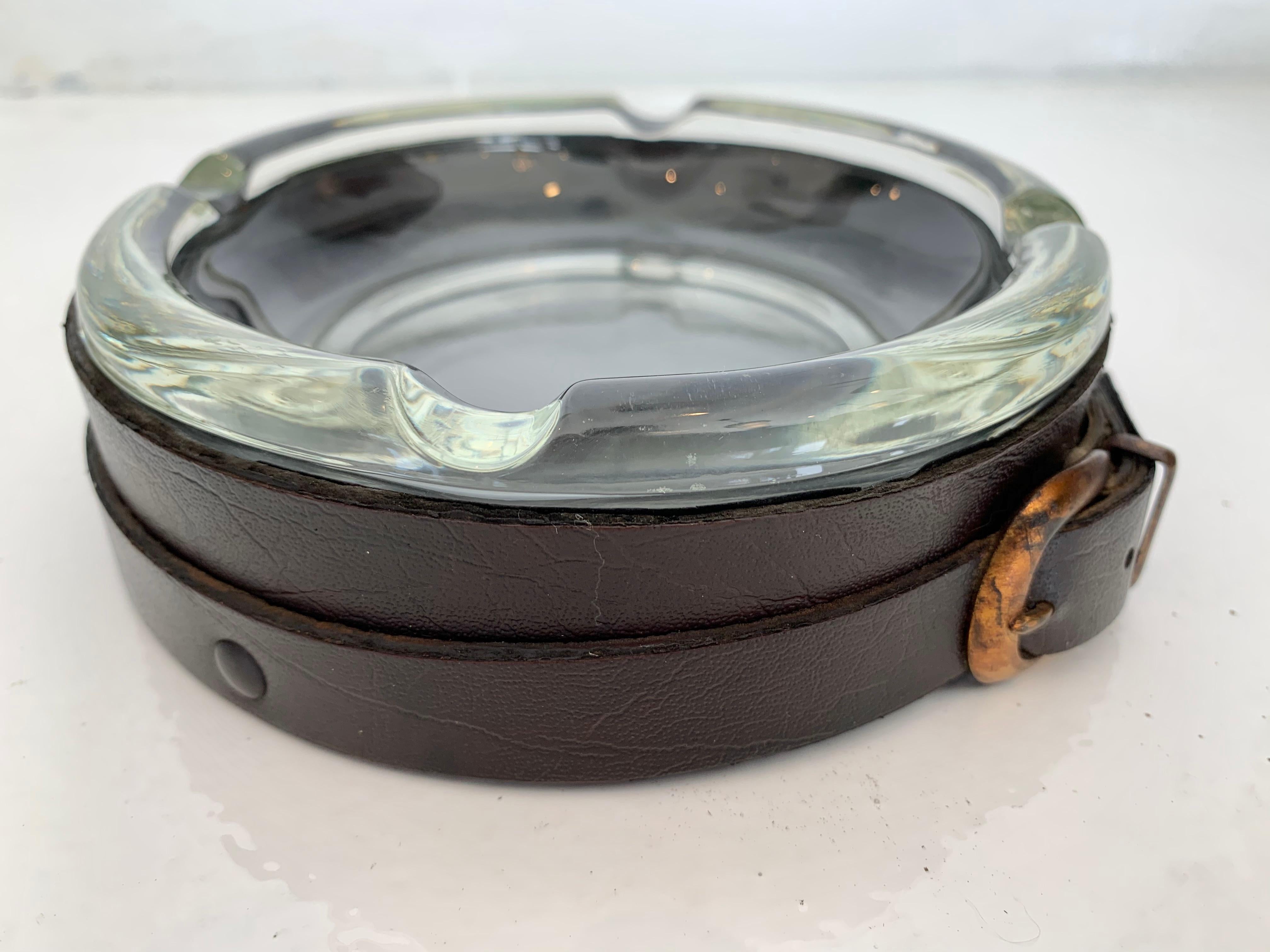 Leather and glass catchall / ashtray in the style of Jacques Adnet. Leather case with strap belt and brass buckle. Glass inset dish. Dish can be removed for cleaning. Good vintage condition. Perfect for keys/objects by the front door.