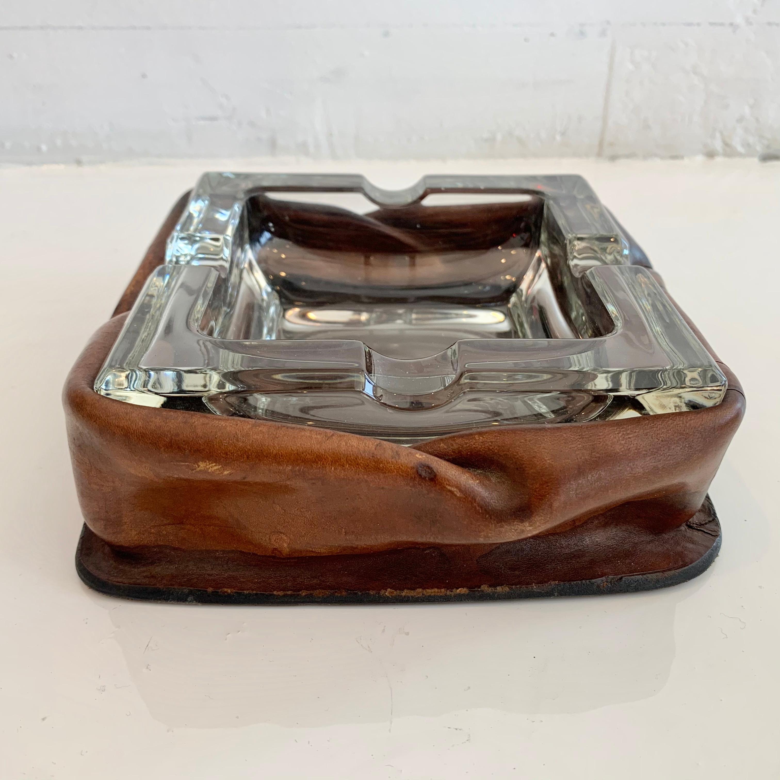 Unique leather and glass ashtray in the style of Jacques Adnet. Rouched saddle leather holds a square inset glass ashtray. Interesting design.