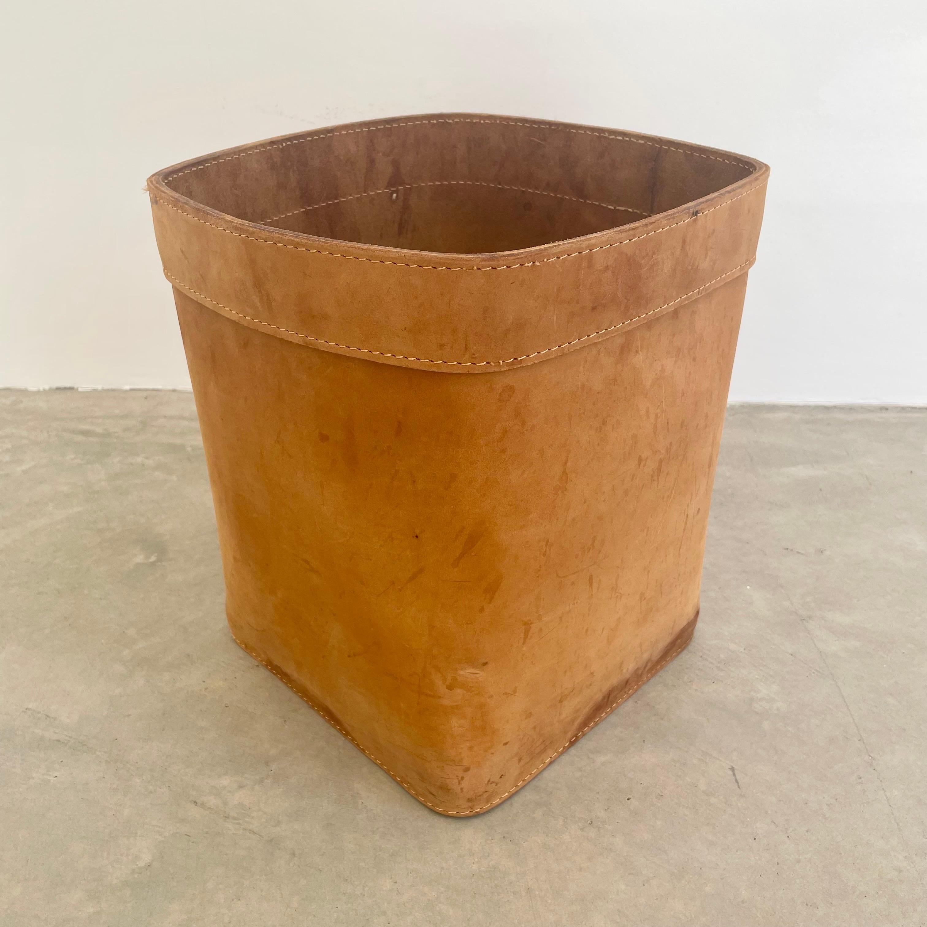 Substantial tan saddle leather waste bin in the style of Jacques Adnet. Circa 1960s. Handmade and hand-sewn from thick top hide leather in a cube shape with a leather base. In good condition with nice patina on the leather. Great color and age.
