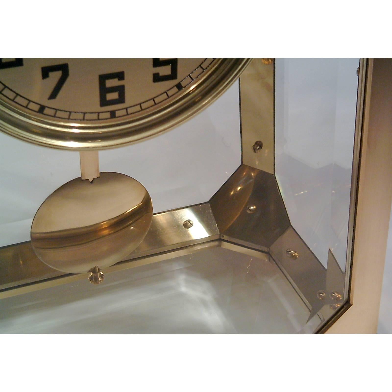 Orologio da tavolo, spesso utilizzato da Adolf Loos nelle case da lui progettate. Struttura in ottone fuso su quattro gambe romboidali, bordi rinforzati che conducono a cornici laterali ottagonali, vetri sfaccettati, sportello anteriore