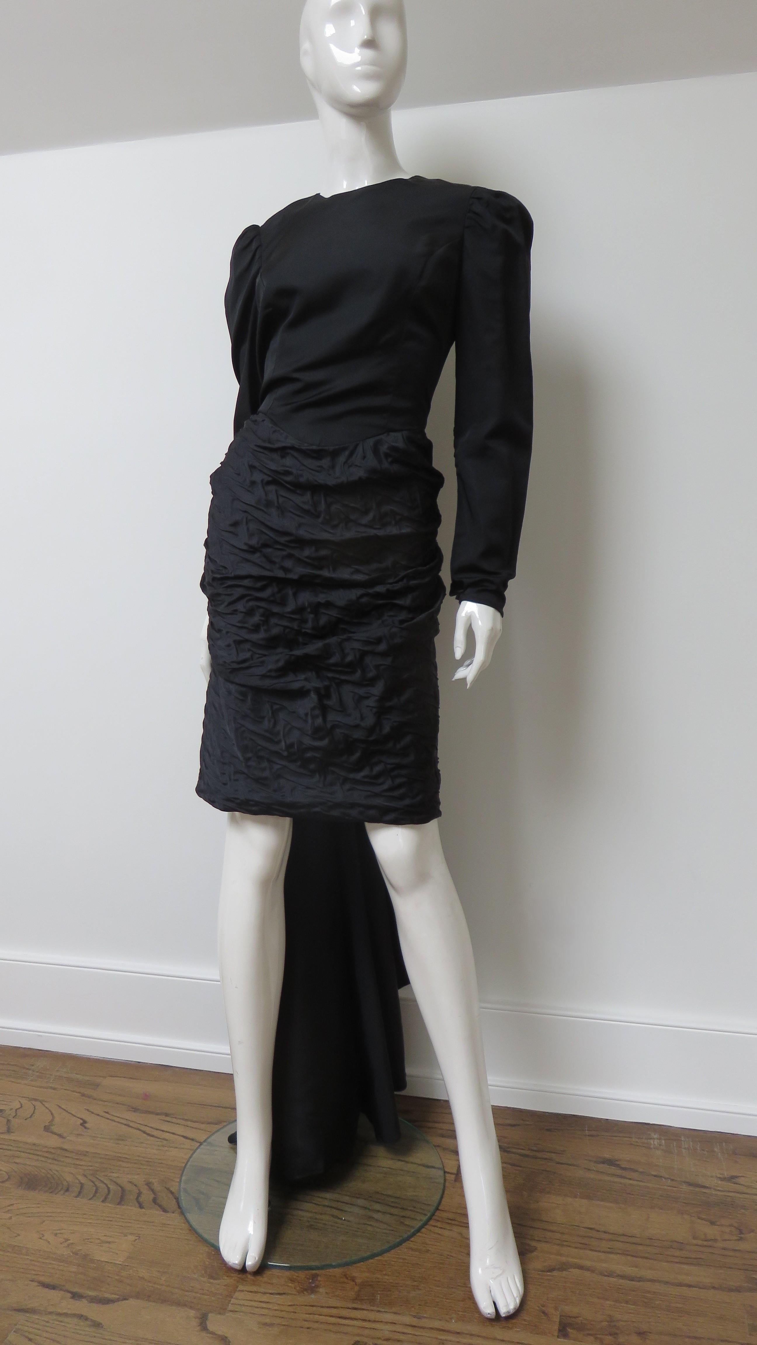 A fabulous black silk dress from Adolfo. It has a crew neckline with a wrap V back bodice, full shoulder long sleeves with snap cuffs, a textured horizontally ruched pencil skirt with a back vent and a floor length back swag from the waist. It has a