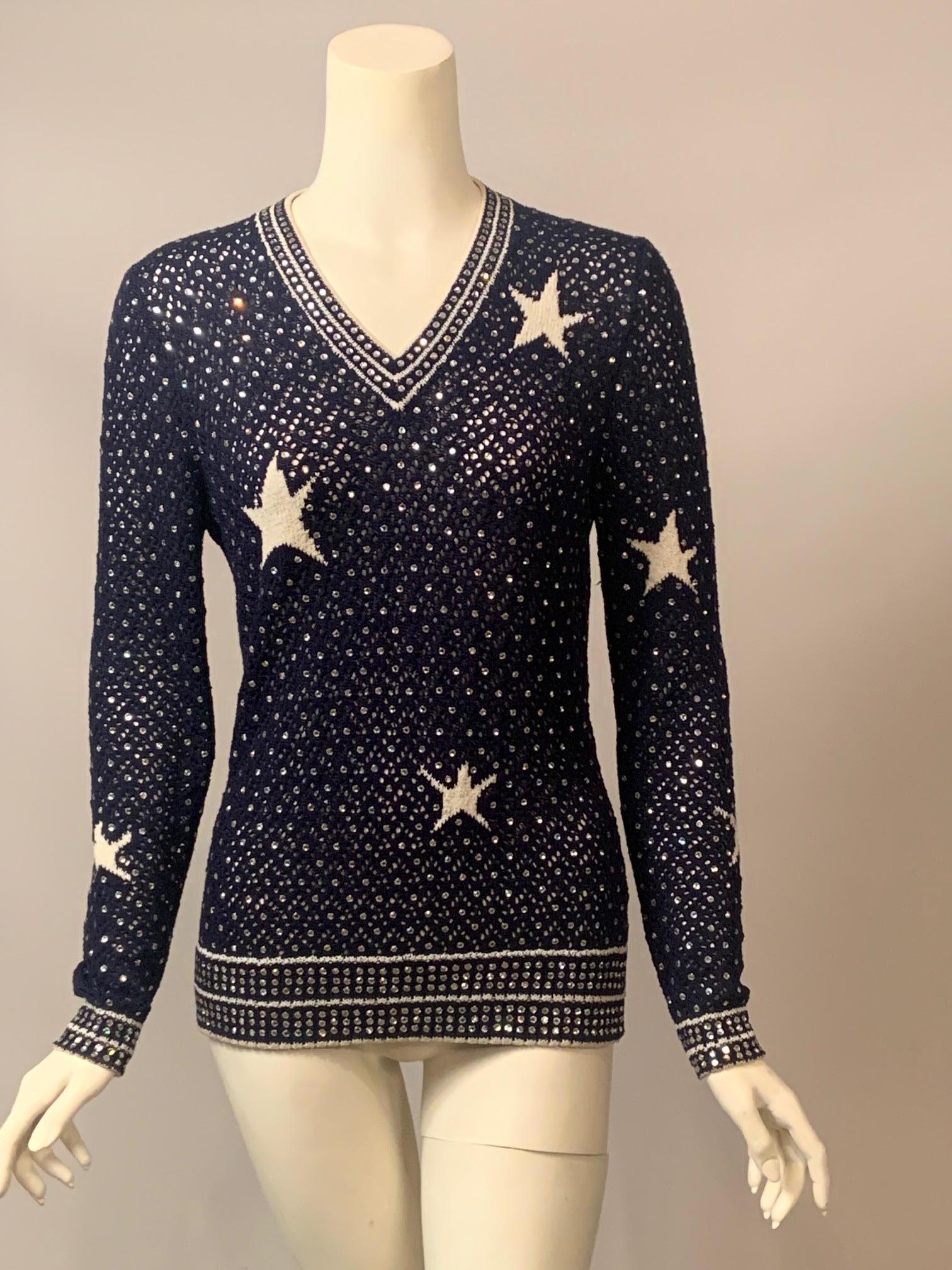 Que diriez-vous d'ajouter un peu d'éclat à votre garde-robe avec ce pull en crochet bleu marine d'Adolfo at Saks Fifth Avenue, orné de strass et d'étoiles en tricot blanc. Le pull a une encolure en V et deux rangées de strass sertis séparées par des