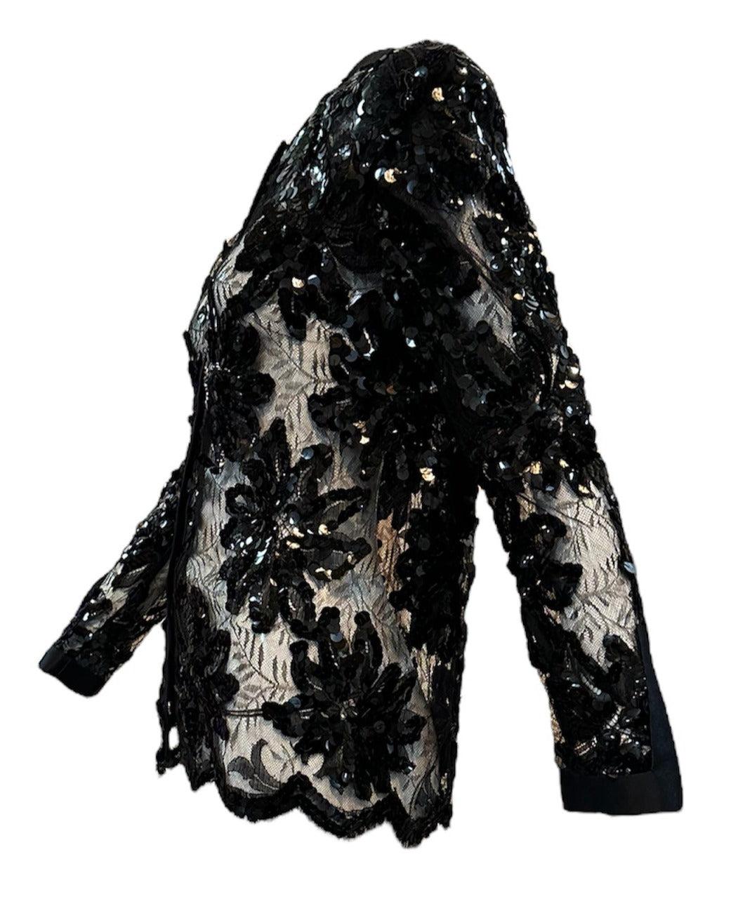 Adolfo 80s Black Chantilly Evening Jacket ist ein echtes Vintage-Stück. Mit ihrer zarten Chantilly-Spitze mit Satinbesatz und einer übergroßen Paillettenverzierung ist diese durchsichtige Jacke perfekt, um jedem Abendoutfit einen Hauch von Eleganz