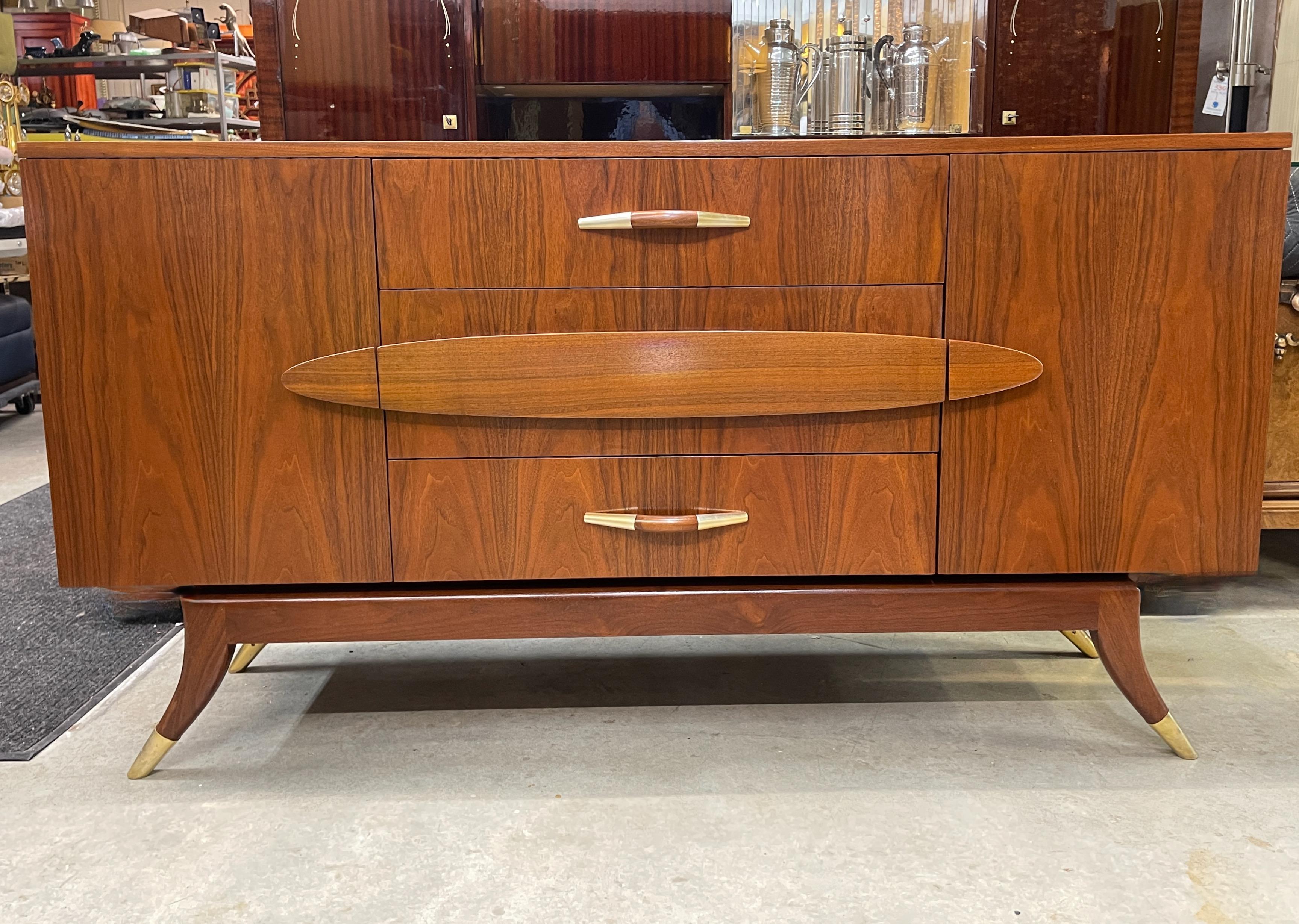 Walnut credenza custom made in 1954 by the Cambridge, MA workshop of F & G Handmade Furniture lead by Adolfo Genovese. 
Rectangular case supported on four curved tapered legs with hand cast solid brass sabots. 
Intense graining and coloring.