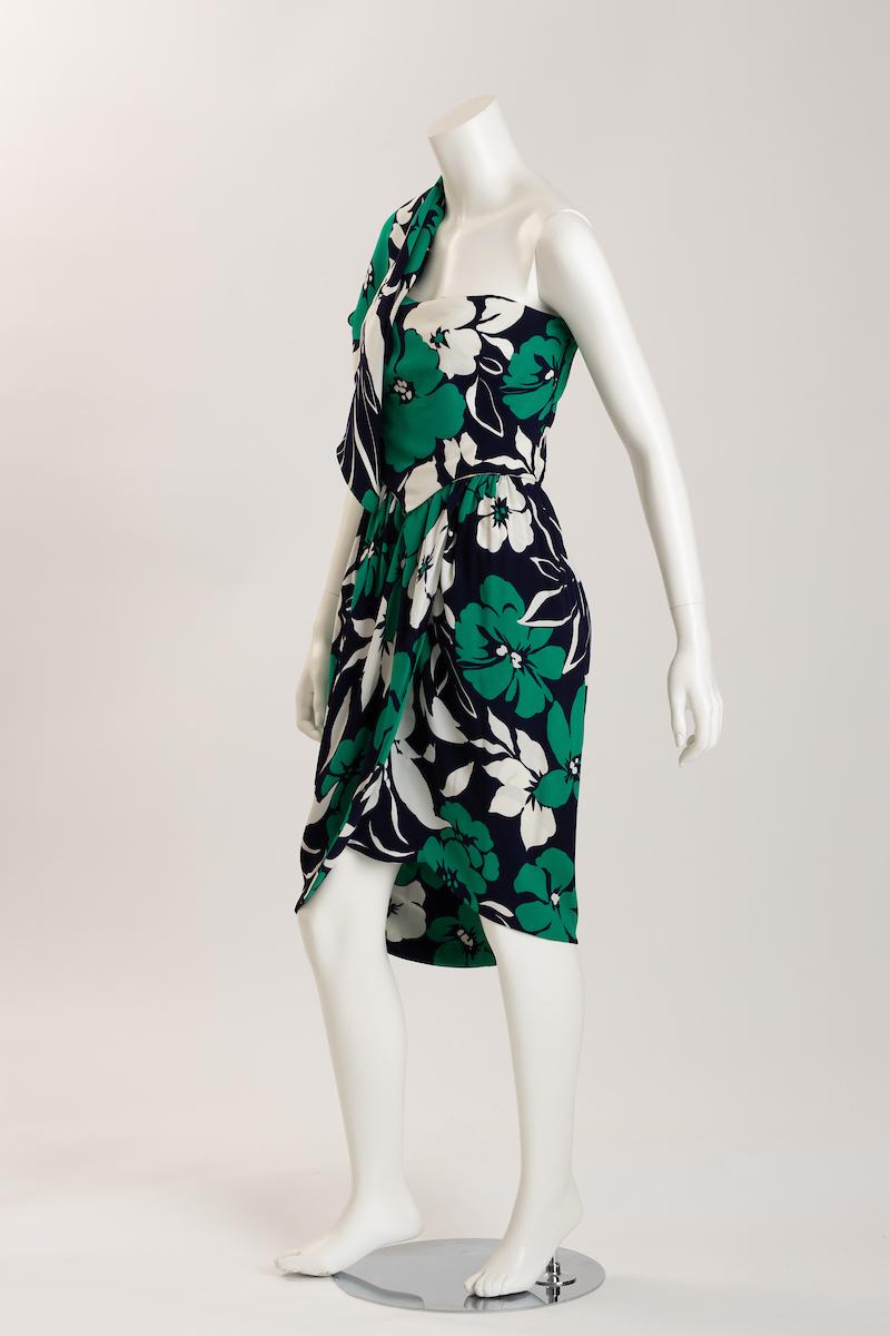 Adolfo strapless dress with bold green, indigo and white tropical floral print. Wonderfully tailored,
 with fitted bodice and draped open tulip front slit above the knee for movement 
Half capelet drapes over one shoulder gives a glamorous and