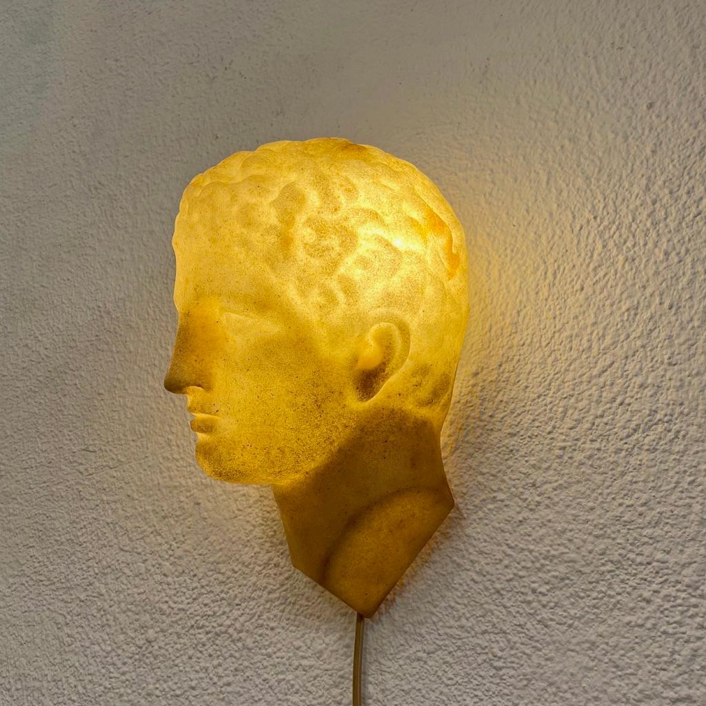 Espléndida y rara lámpara de pared del rostro del bello varón griego Adonis, realizada en fibra de vidrio con acabado de polvo de mármol creada por el diseñador francés André Cazenave, muy conocido por sus creaciones de lámparas de roca lunar