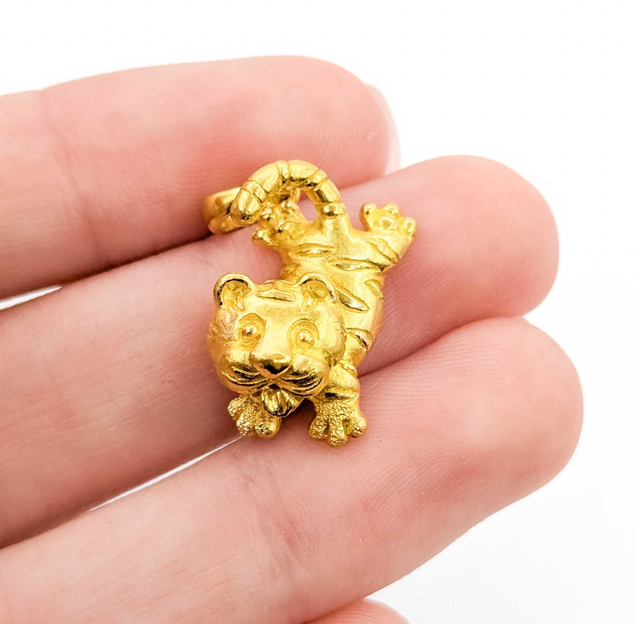 Charmant et magnifiquement détaillé, ce pendentif chaton tigre est réalisé en or jaune 24k avec une pose enjouée et des traits expressifs. La finition high-karat donne à la pièce un éclat chaud et riche qui met en valeur sa texture sculptée et son