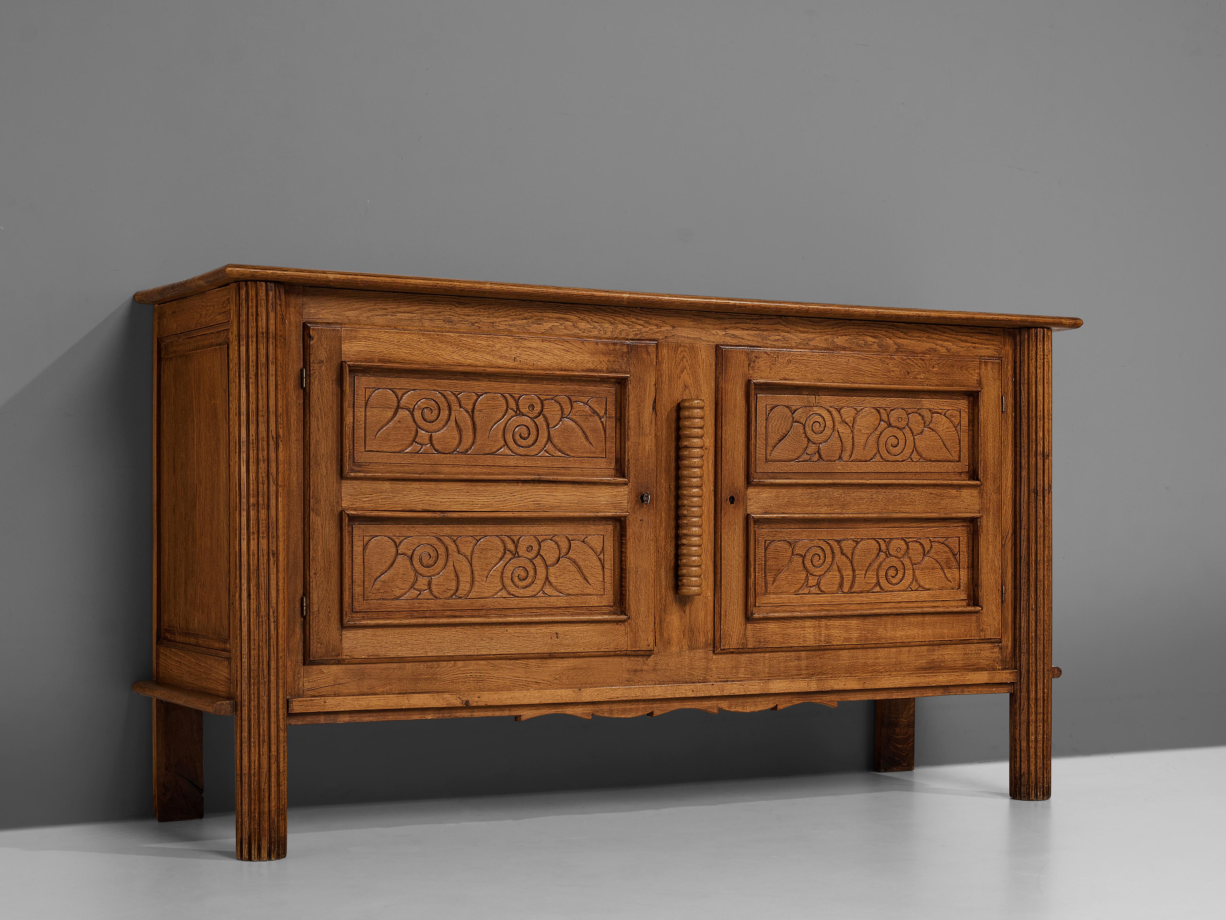 Sideboard, oak, France, 1940s

Beautifully decorated sideboard in a late art deco style. The sideboard has gorgeously ornamented doors that have an abstract floral motif. These embellished doors open with keys. The credenza stands on column-inspired