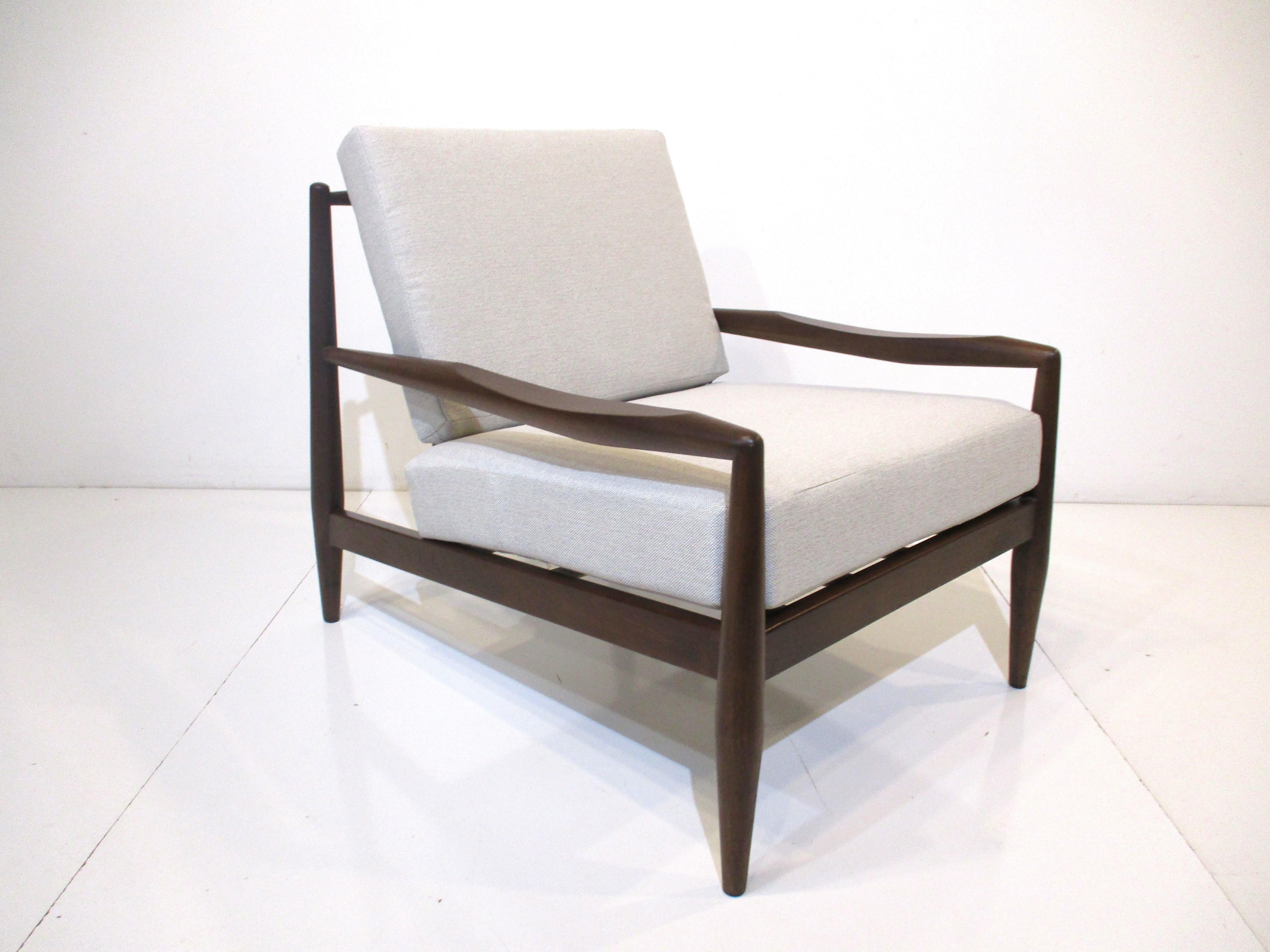 A solid dark walnut very well crafted sculptural framed lounge chair with two loose cushions upholstered in a tight woven beige and cream fabric . The arms have a scooped out rest , tapered legs and dowel backside with a nice depth for maximum