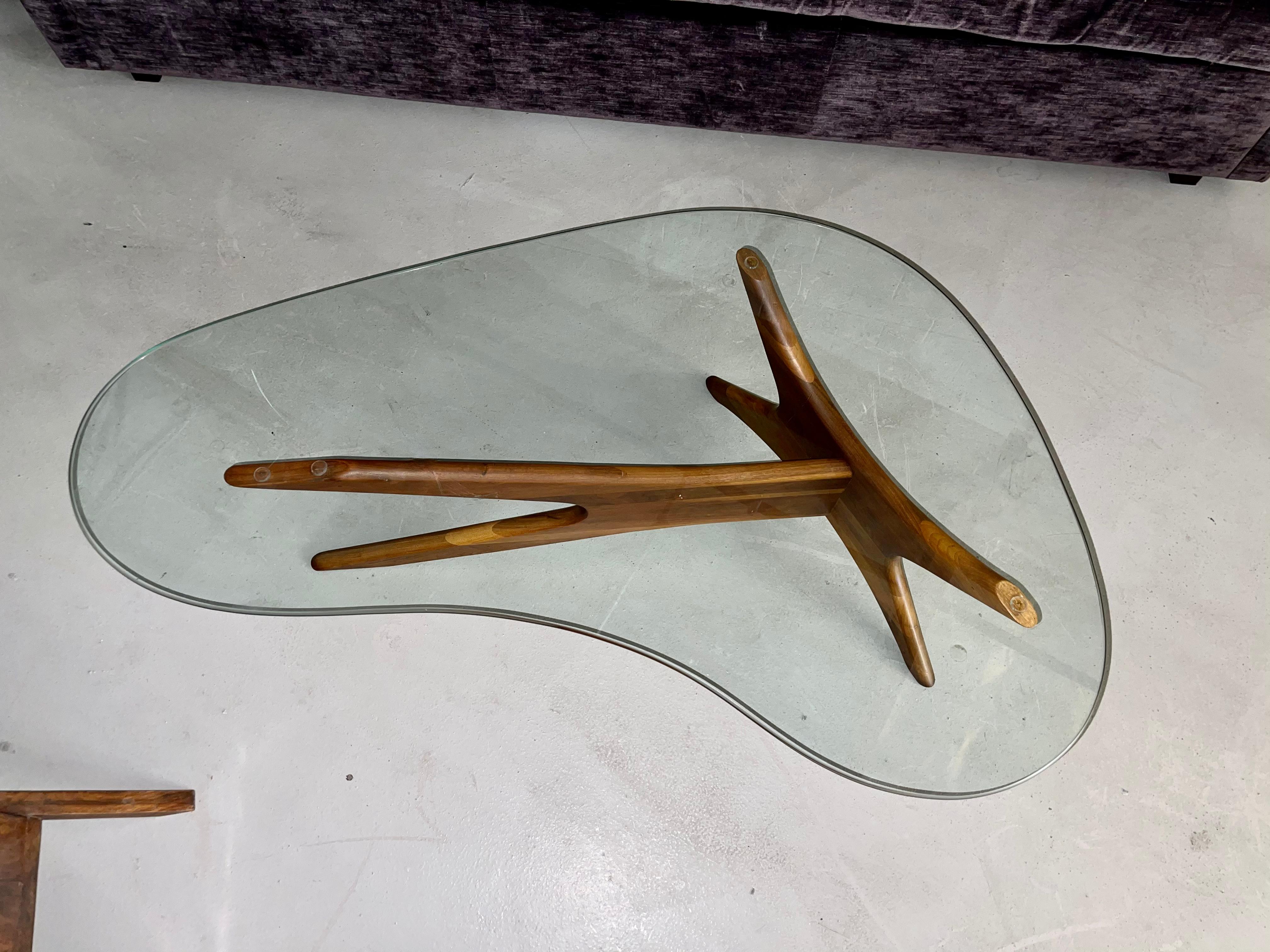 A glass top walnut base kidney shaped table by Adrian Pearsall. Nice vintage condition. The wood base is good and the glass is good with a few minor marks to the surface.