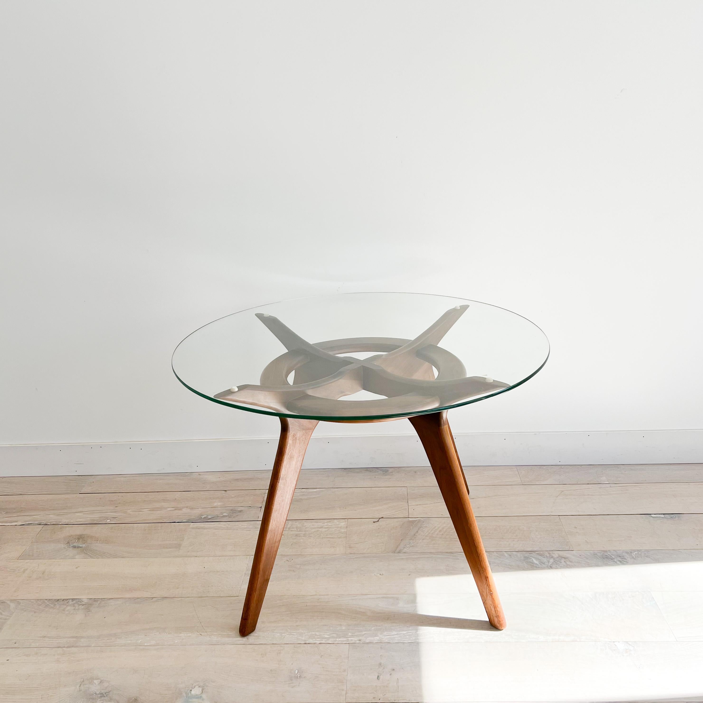 Mid century modern dining table with sculpted walnut base and round glass top by Adrian Pearsall. Known as the Compass table. Some light scuffing/scratching to the glass top. Some scuffing/scratching to the wooden frame.

42” Diameter - 29” High