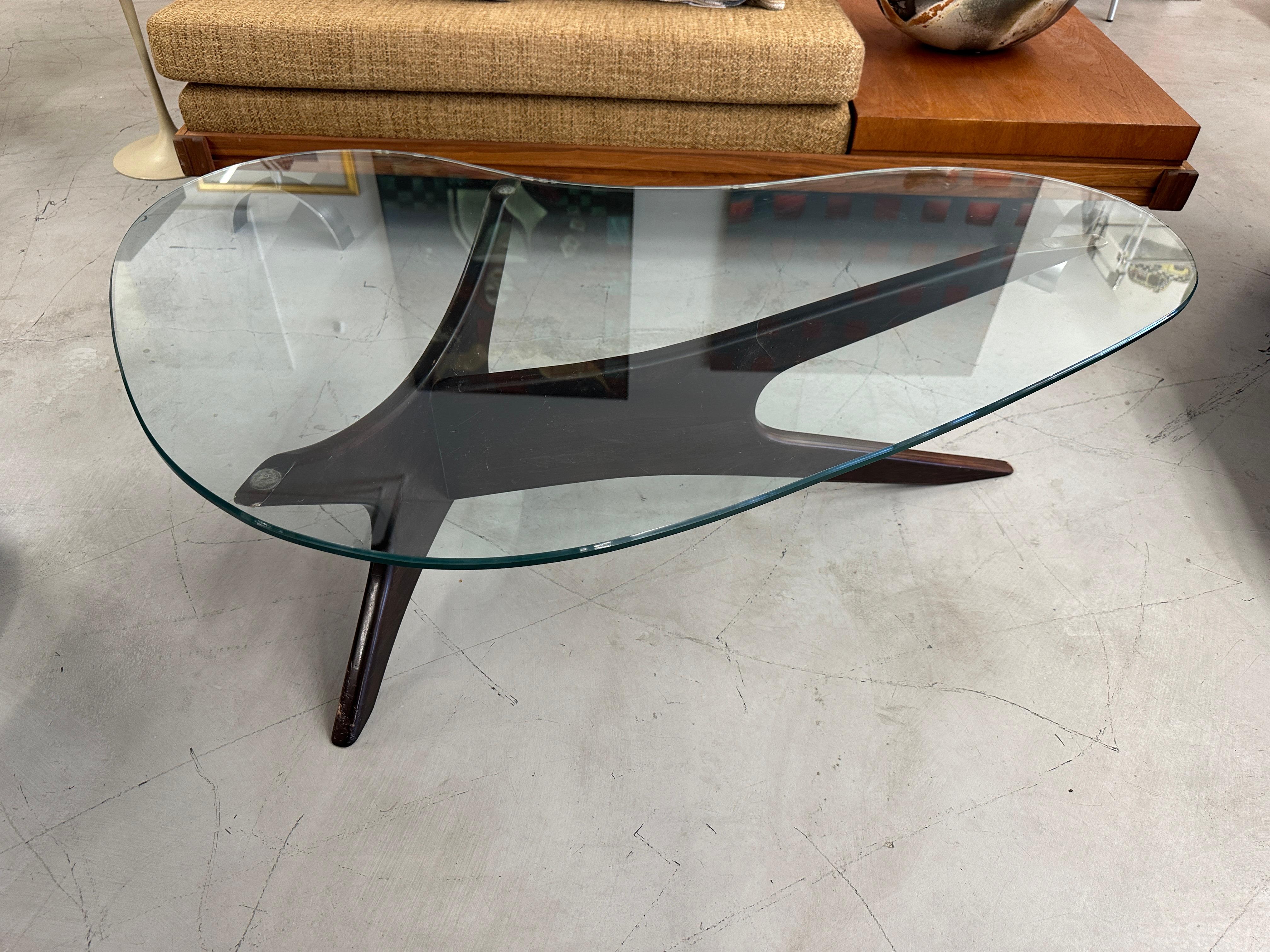 A nice iconic coffee table by Adrian Pearsall for Craft Associates. The top has a biomorphic kidney shaped piece of glass. The glass is in good condition with a few minor surface scratches. No edge chips. 
The base has some wear and nicks, scuffs