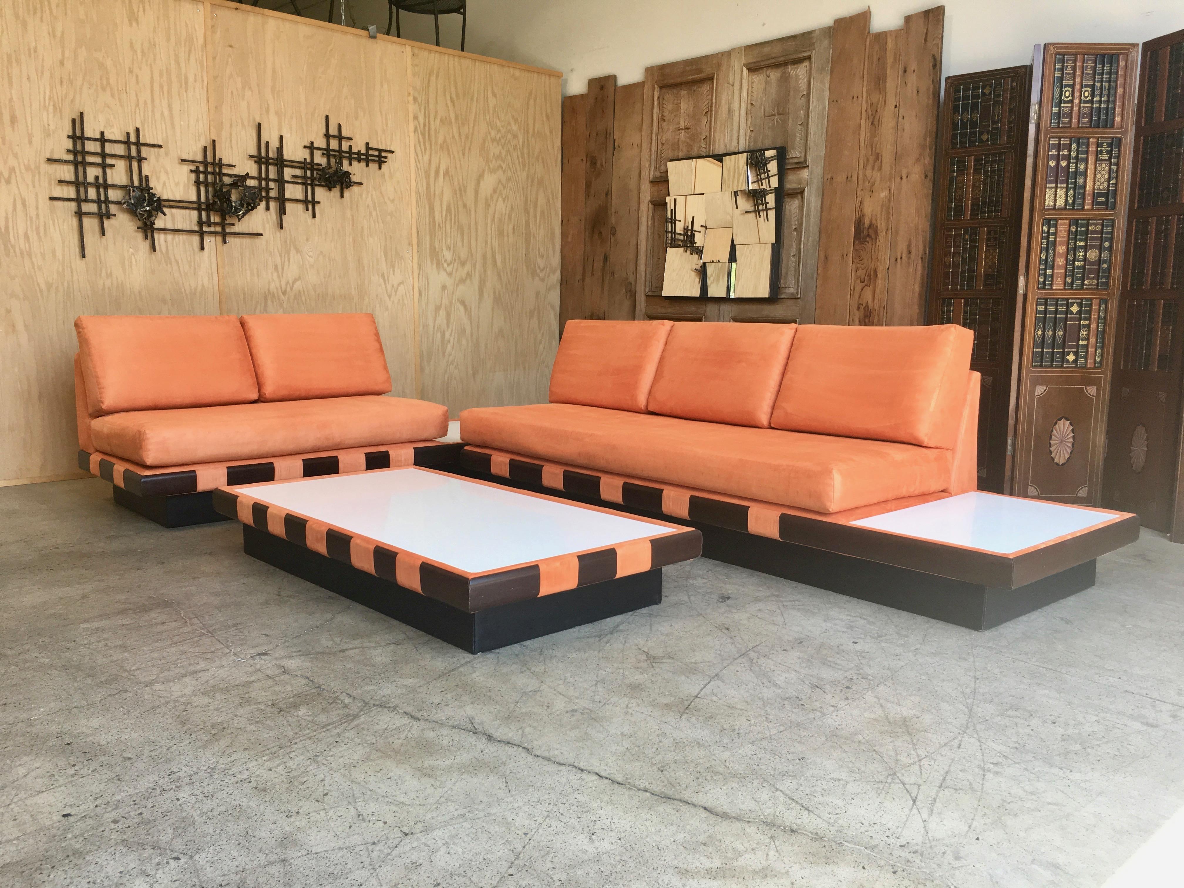 Three-piece set with one three seat, one two seat and one coffee table
recently recovered in orange micro fiber with white quartz table tops and black vinyl plinth.
The three-seat is 103.5