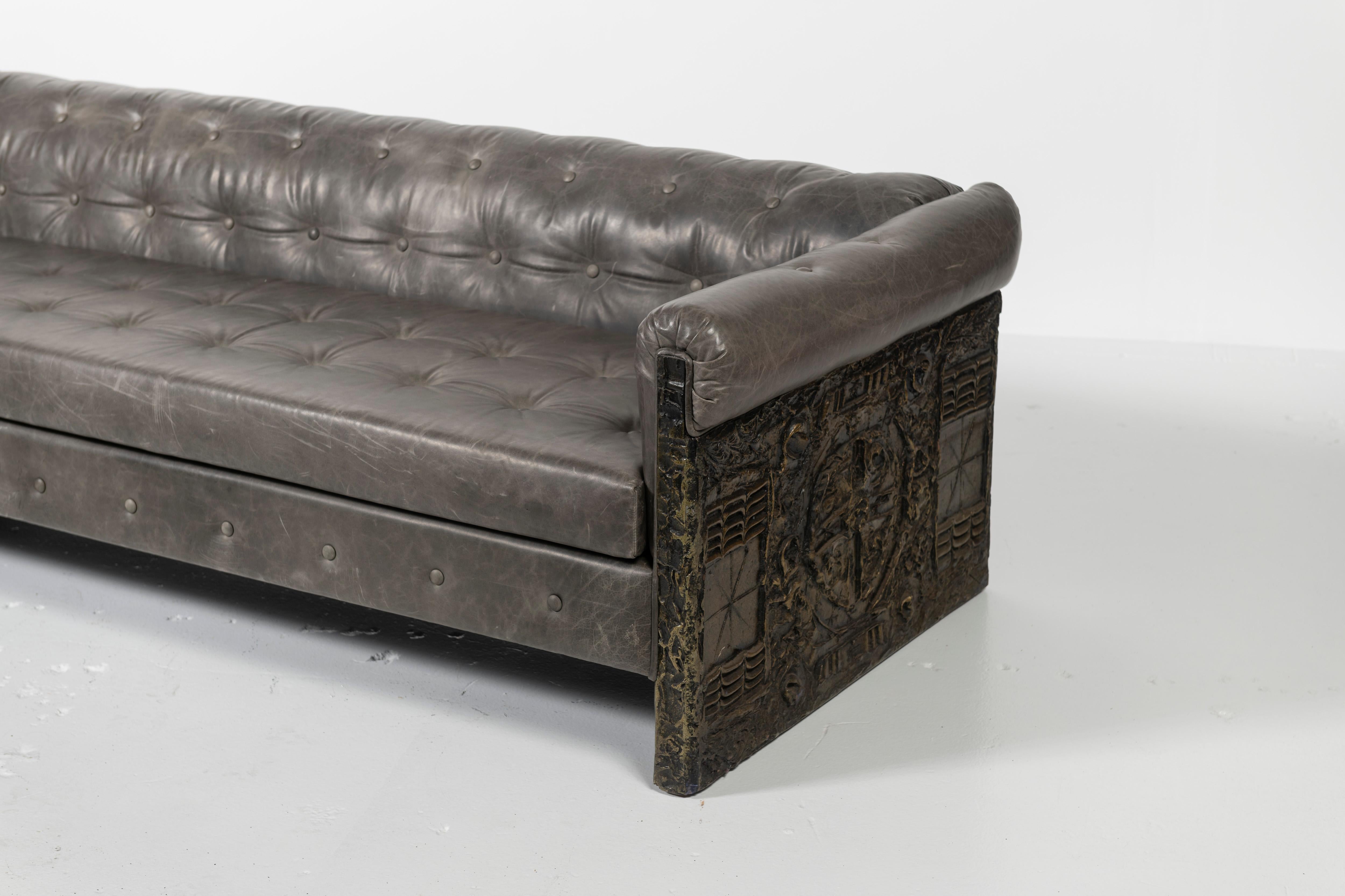 Highly desired Adrian Pearsall sofa, this button-tufted gray leather upholstered sofa has molded and bronzed poly-resin panels on the ends in the Brutalist-style. All materials are original. The seat cushion is non-reversible with a block foam